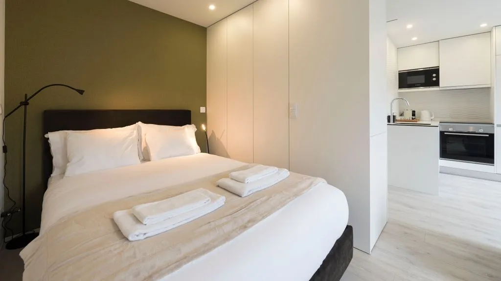A bedroom with a neatly made bed and a compact kitchen visible beside it.