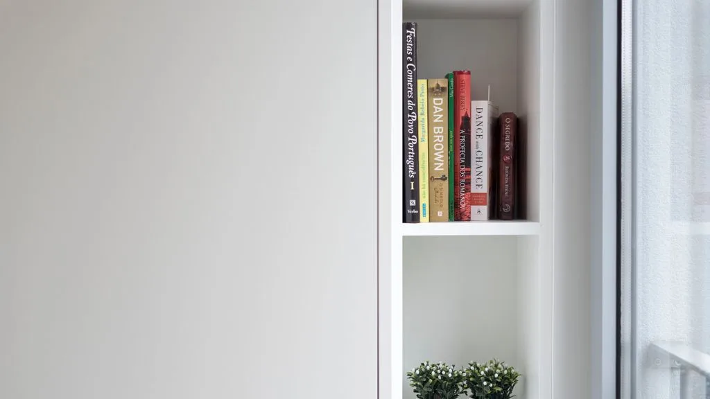 A built-in bookshelf beside a window displays several books and a small plant.