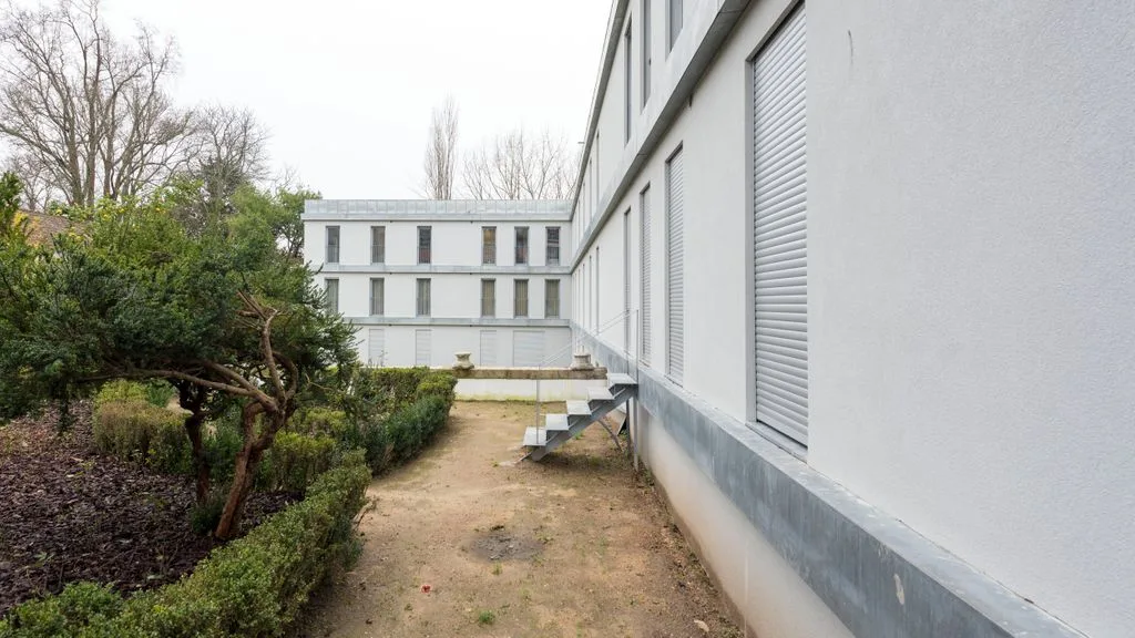 A paved walkway runs beside a modern building and landscaped garden.