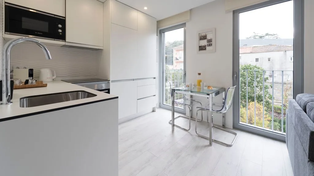 A bright kitchen and dining area with a glass table beside large windows.