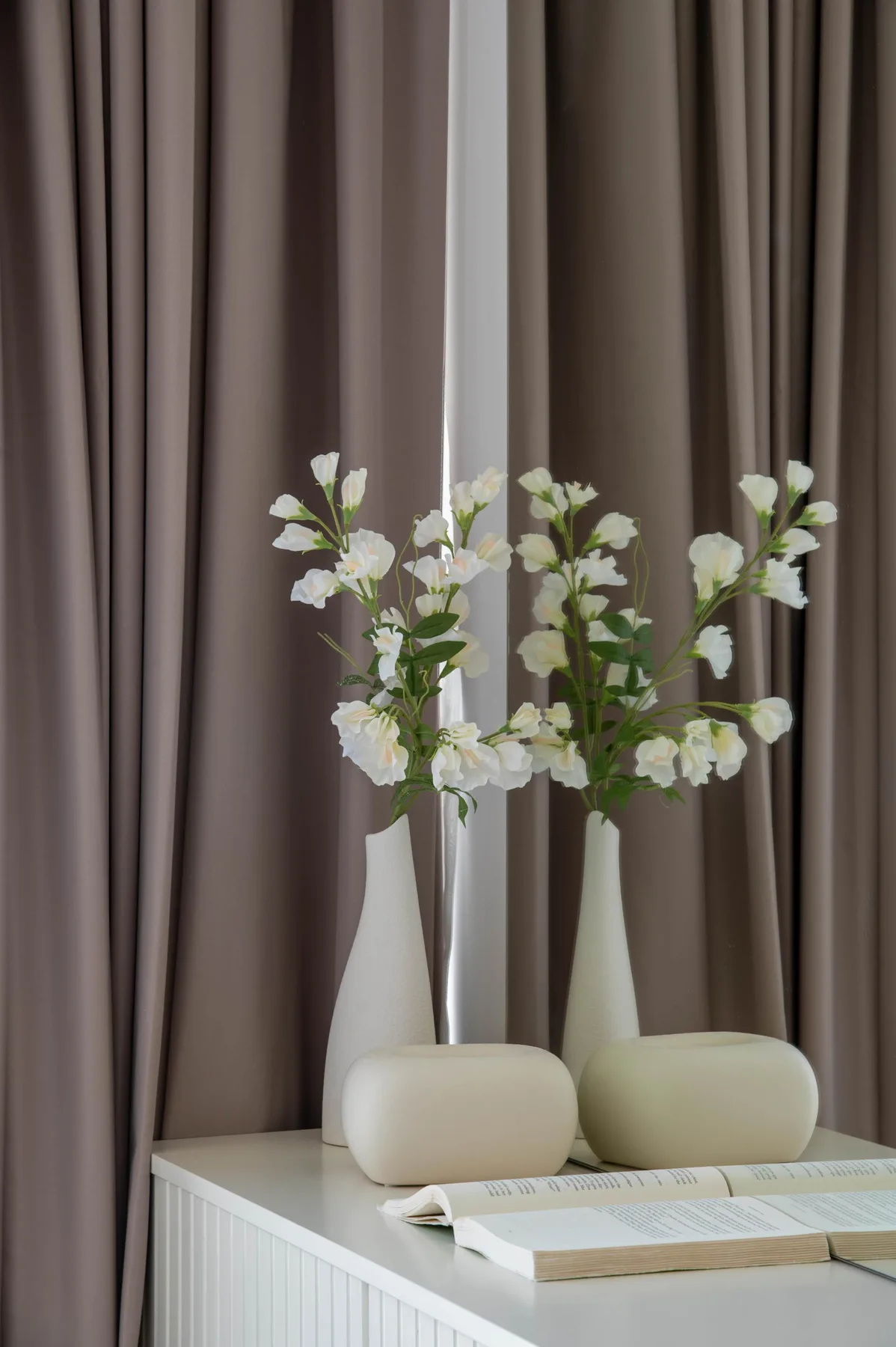 Un arreglo de flores blancas y jarrones sobre una mesa frente a cortinas.