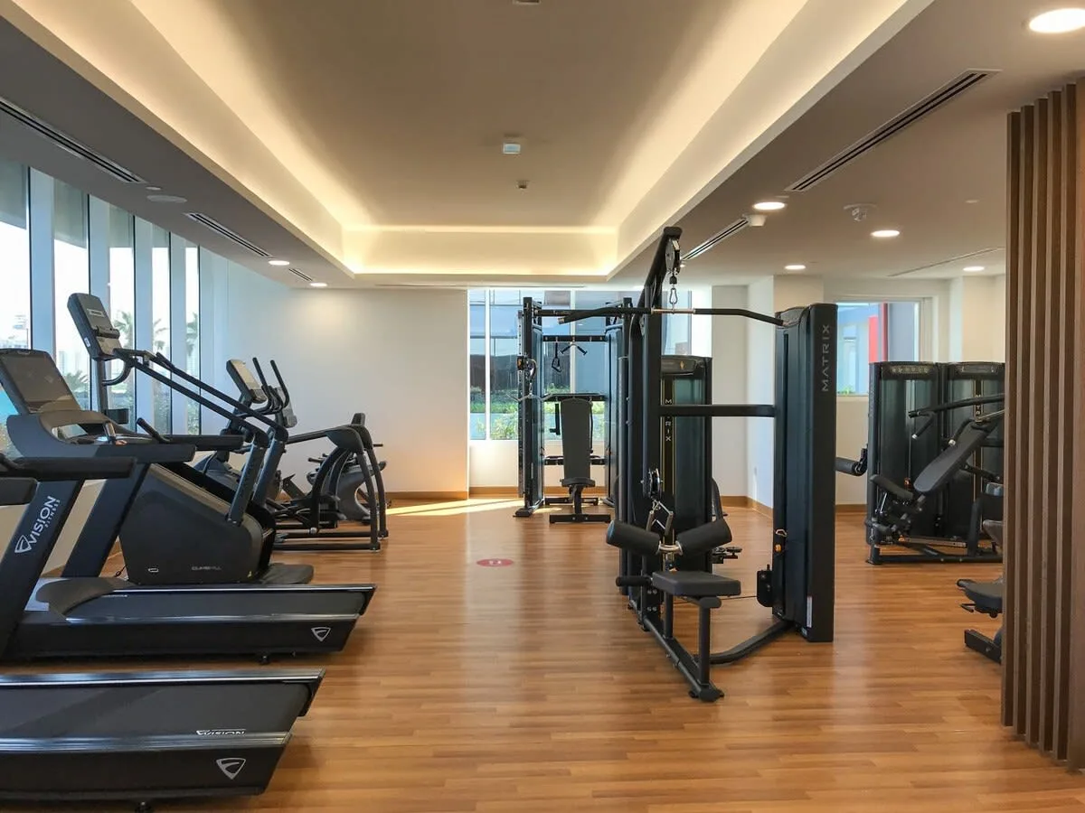 Un gimnasio con cintas de correr y equipos de fuerza distribuidos sobre un suelo de madera.