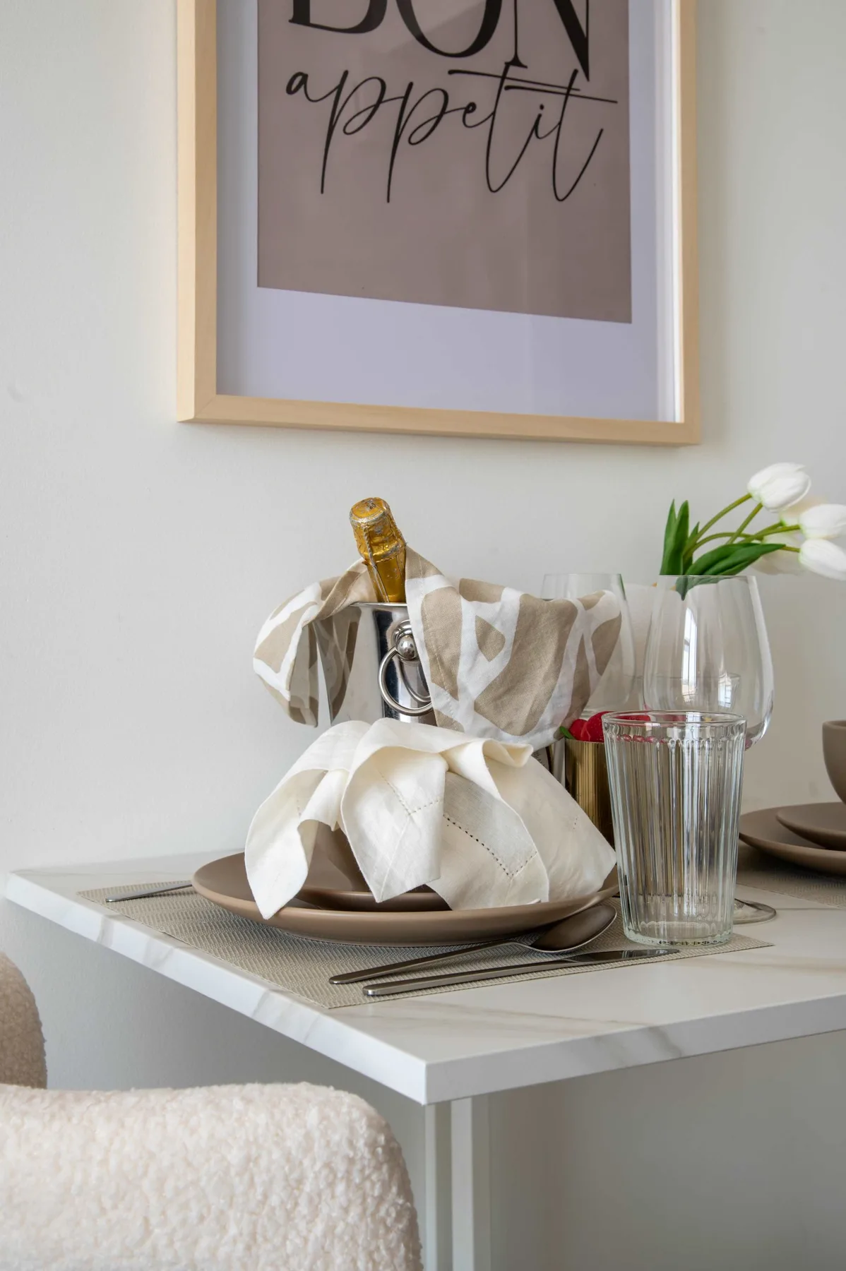 Una mesa de comedor está puesta con platos, vasos, una botella y flores.