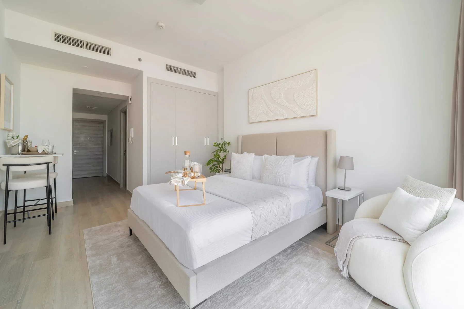 Un dormitorio luminoso con una cama tendida y un sillón de color claro.