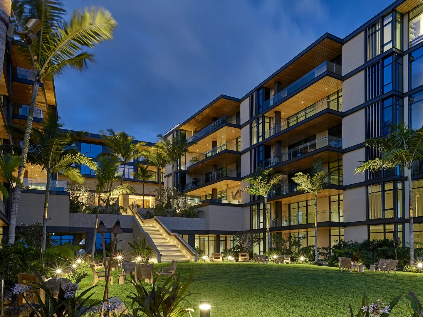 A modern multi-story building overlooks a landscaped courtyard at dusk.
