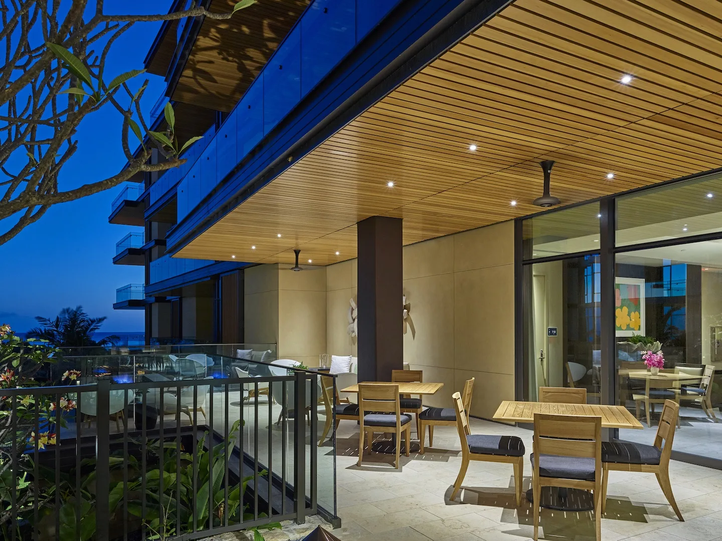 An outdoor dining terrace with tables and seating beneath a wood-paneled overhang.