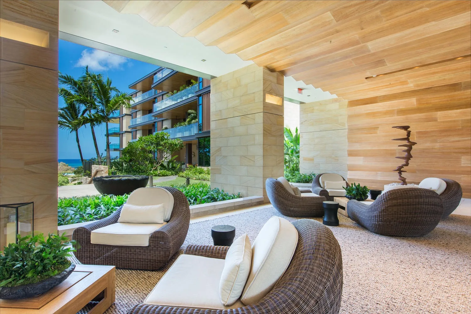 An open-air lounge with woven seating overlooks a landscaped courtyard and nearby building.