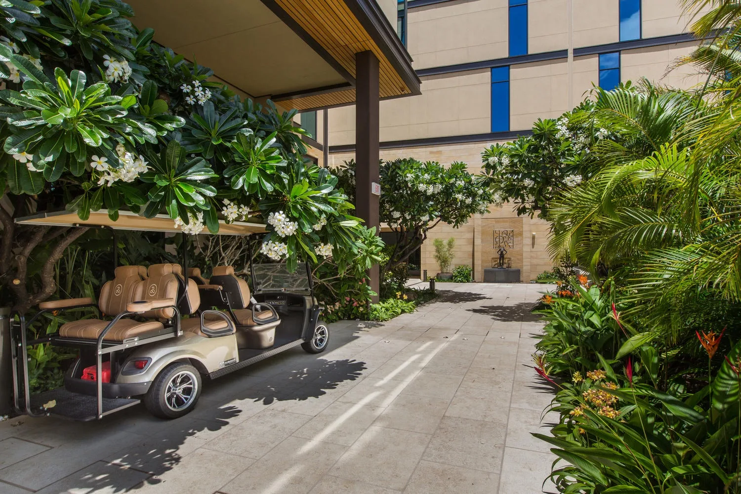 A golf cart is parked along a paved walkway bordered by lush greenery.