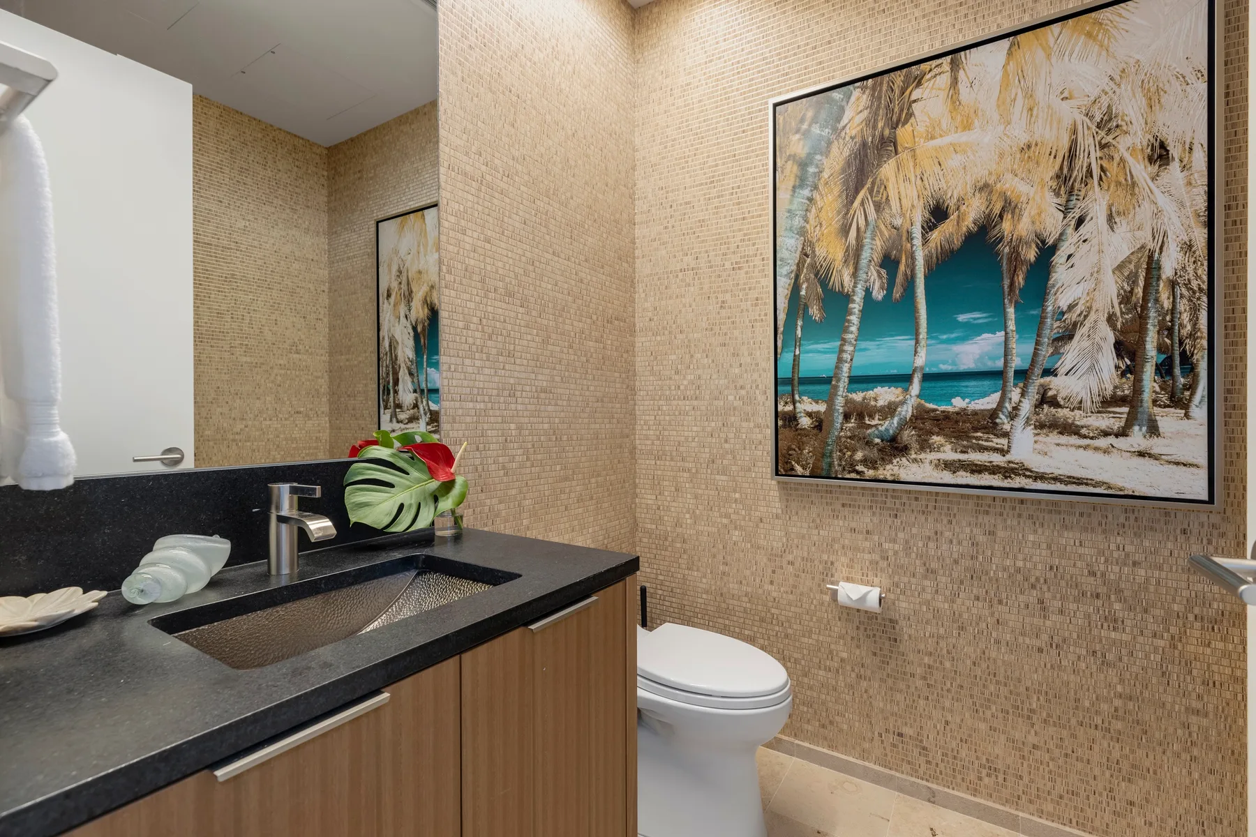 A bathroom with a sink, toilet, and tropical beach artwork on the wall.