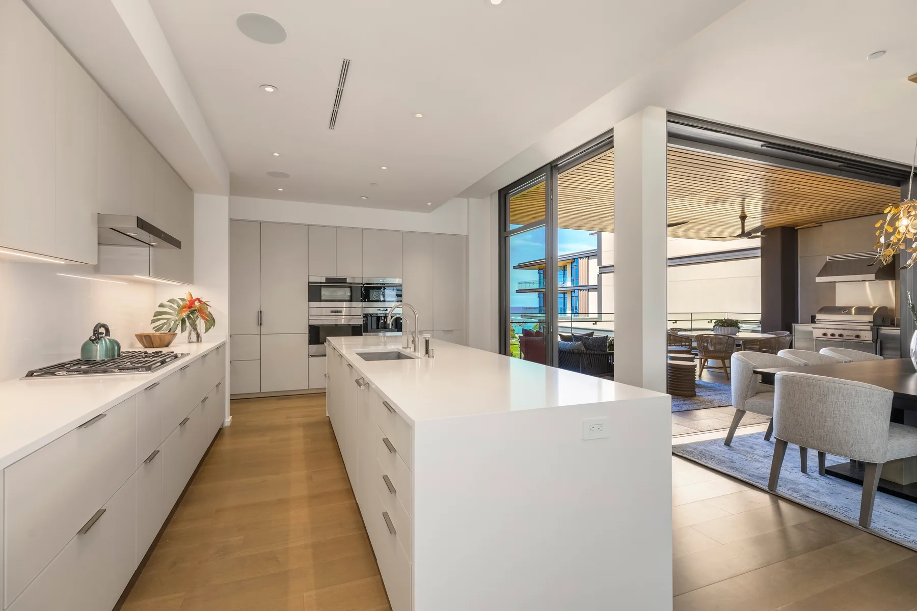 A bright modern kitchen with white cabinetry and a large island opens onto a dining area.