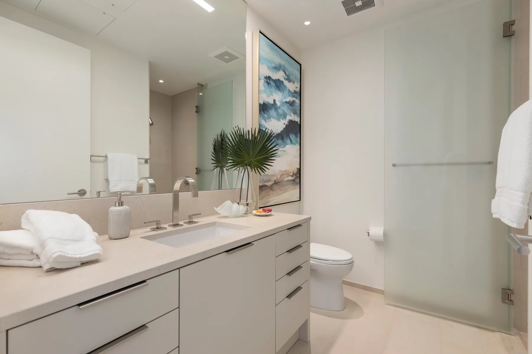 A bright bathroom with a long vanity, mirror, and glass shower.