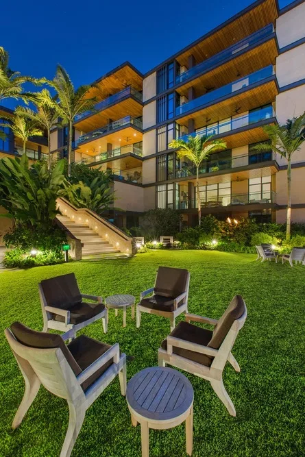 A modern multi-story building overlooks a landscaped lawn with outdoor seating.