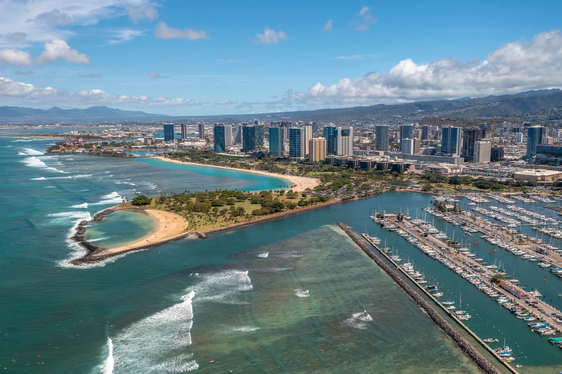 A coastal city skyline overlooks a curved beach and marina.
