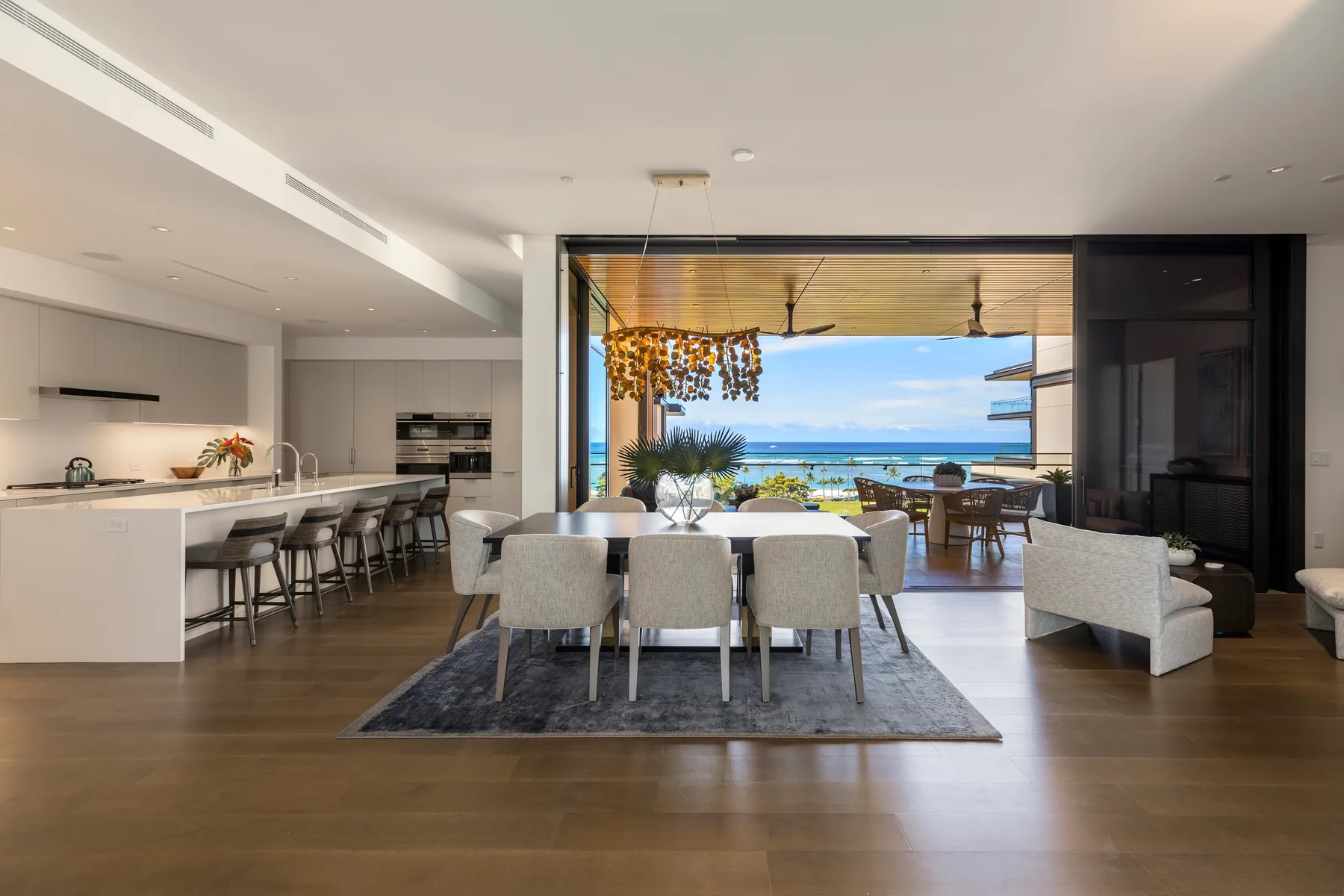 An open-plan dining and kitchen area opens onto a covered outdoor seating area with an ocean view.