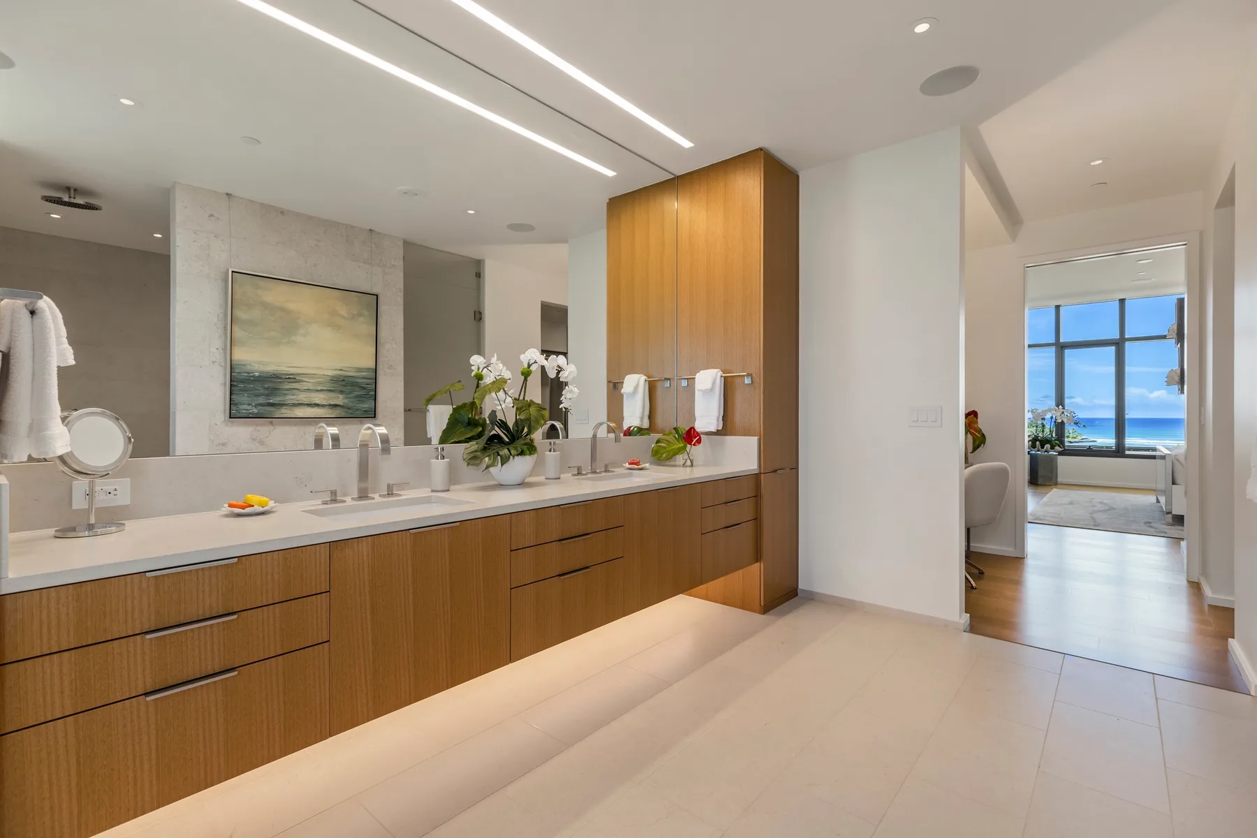 A bright bathroom with a long vanity and an open doorway to a room with ocean views.