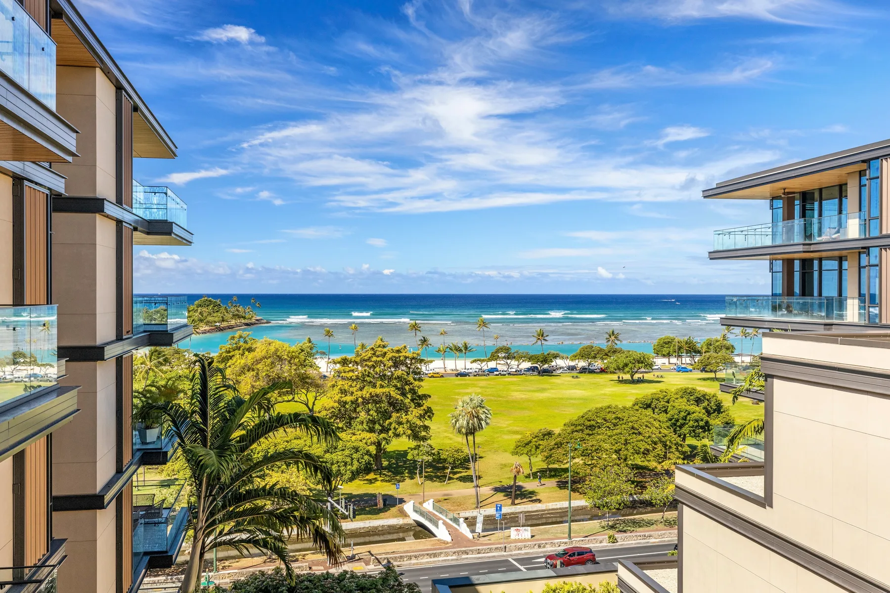 A coastal view between modern buildings, with green parkland and the ocean beyond.