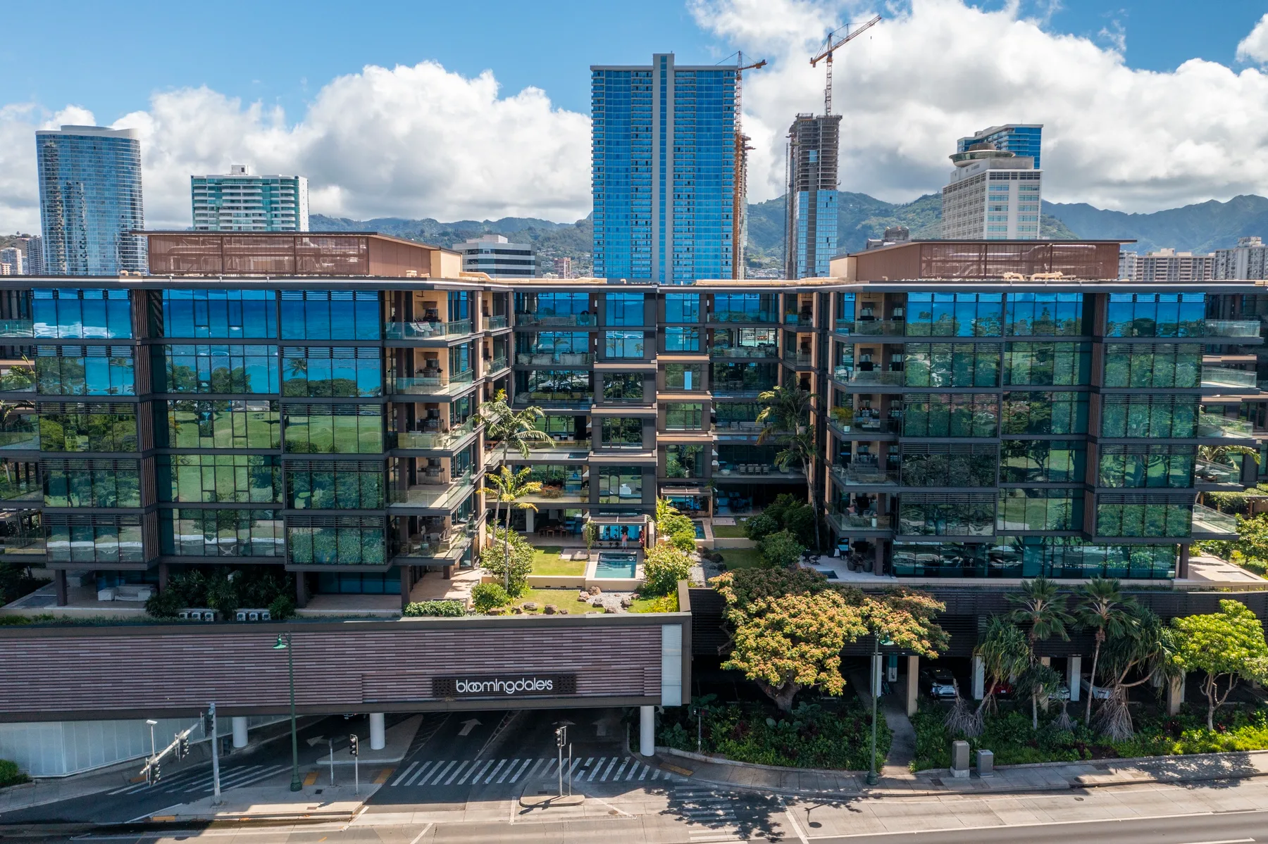A modern glass-fronted building stands before a city skyline and distant mountains.