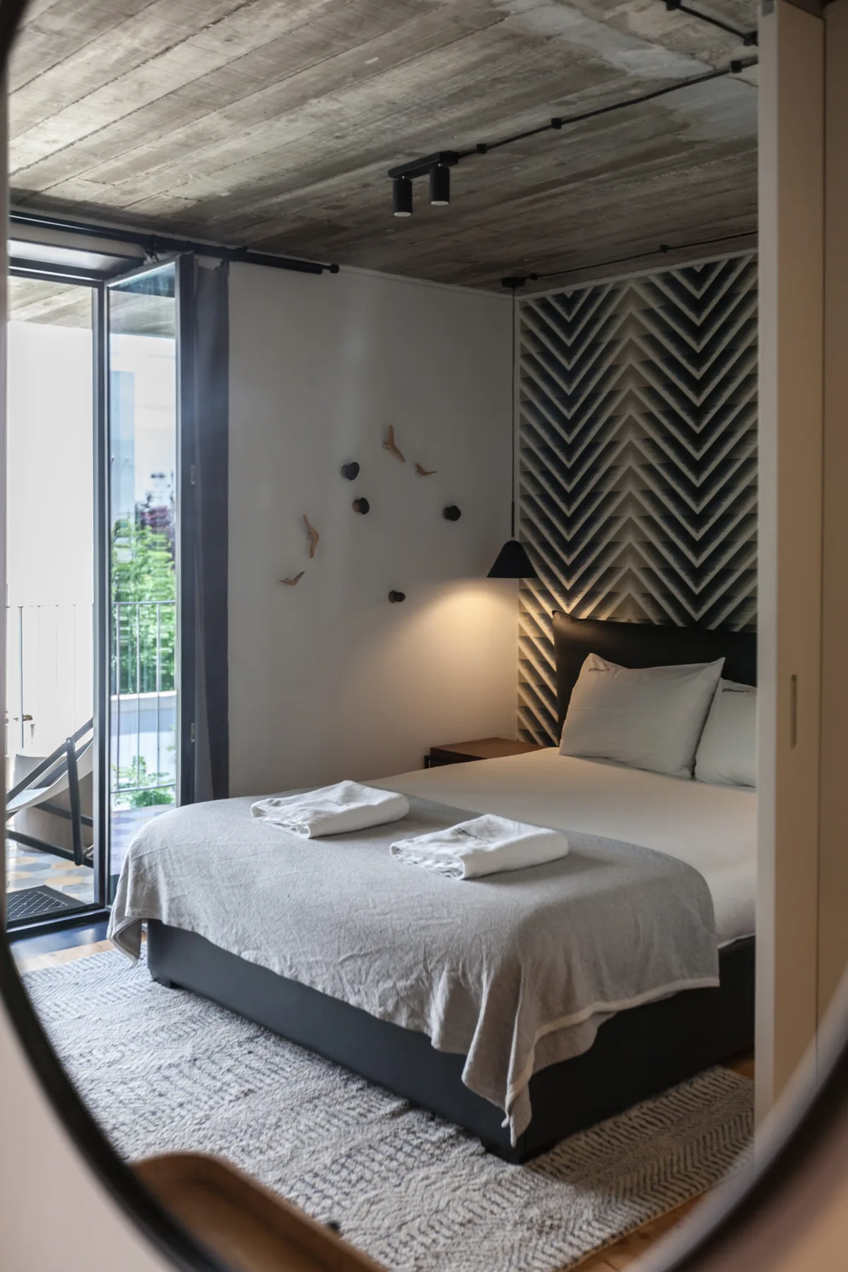 Un dormitorio con una cama bien tendida junto a un panel alto de pared estampado.