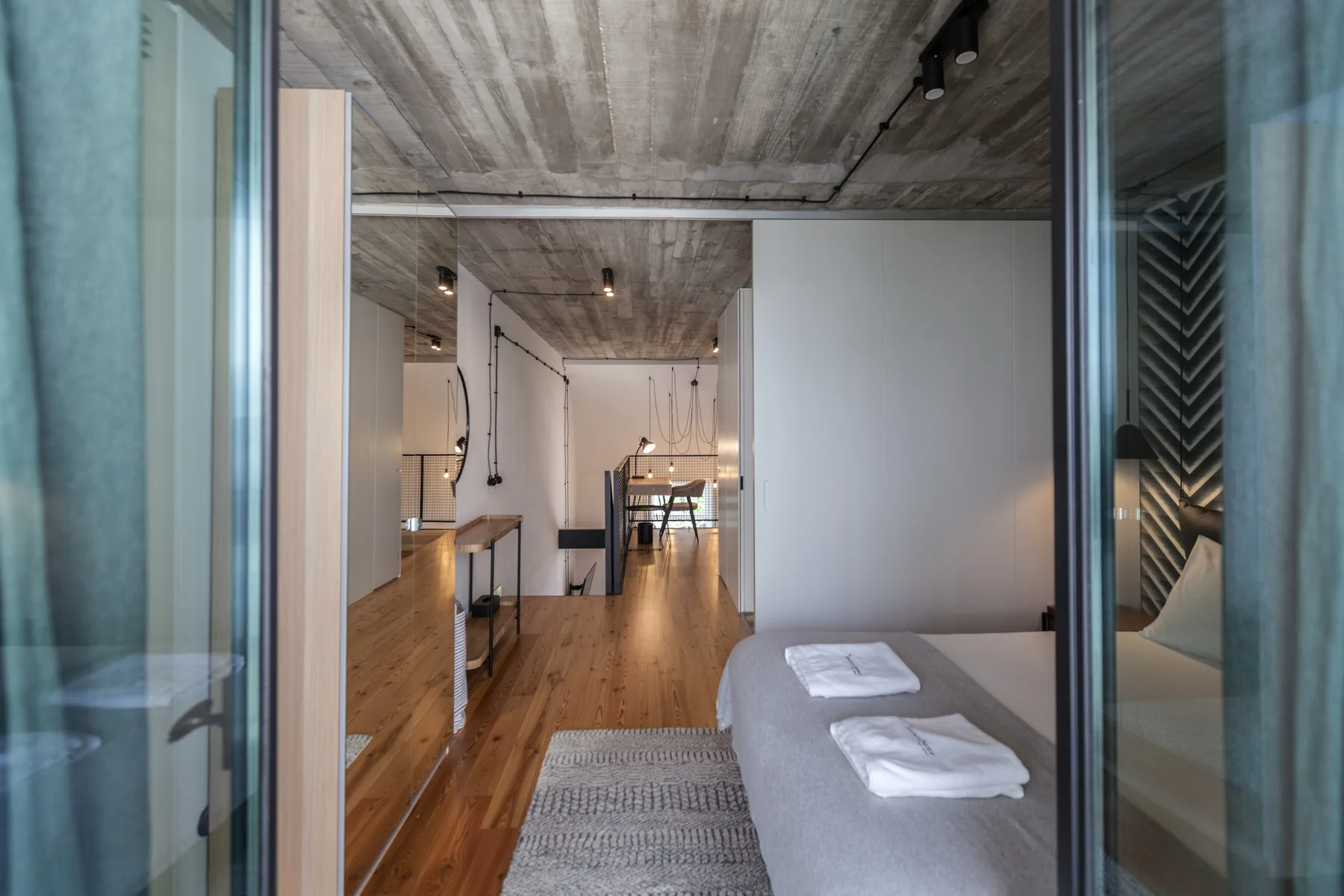 Un dormitorio moderno se abre a una zona de estar con una cama y suelo de madera.