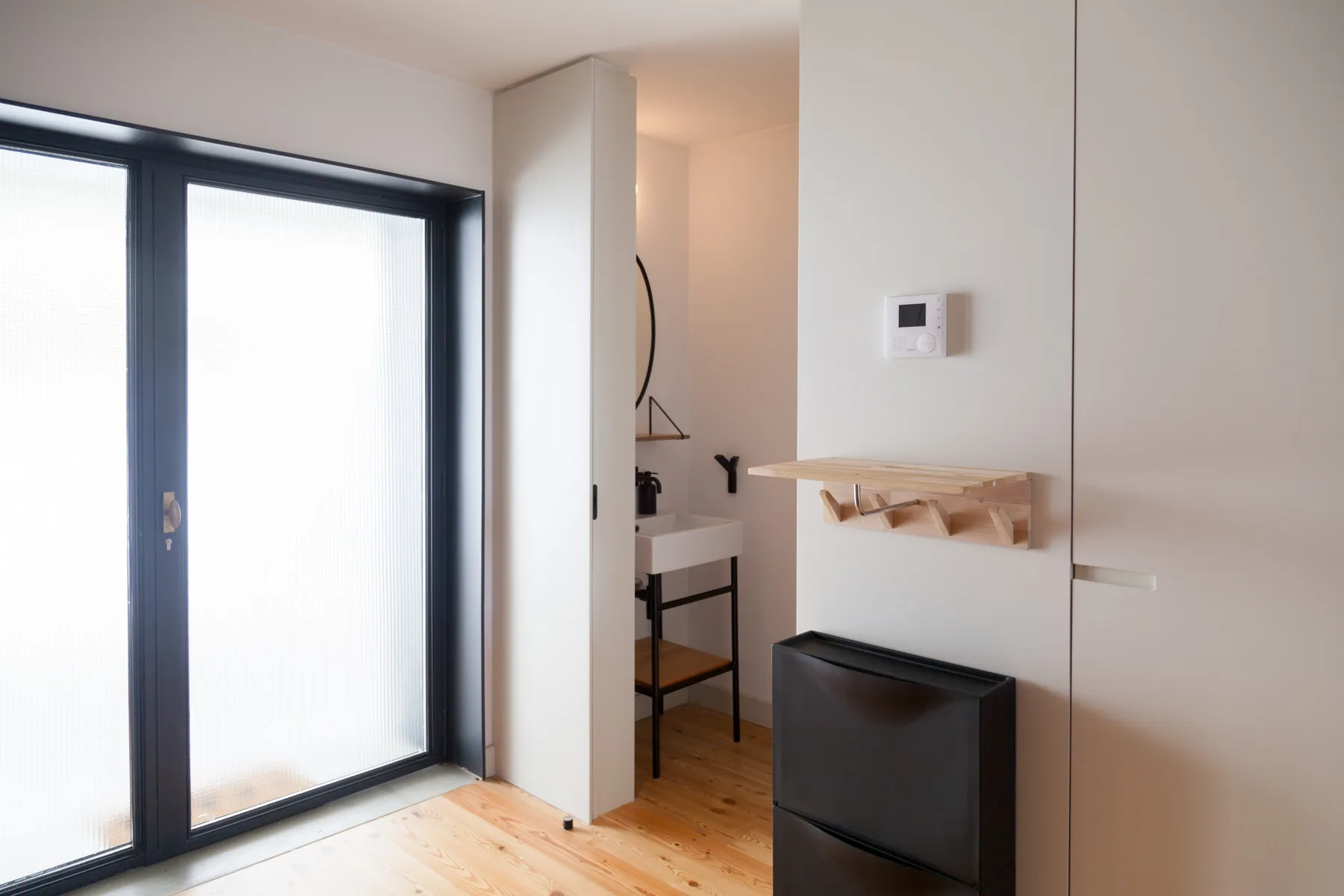 Una habitación luminosa con ventanas grandes, un escritorio pequeño y un estante en la pared.
