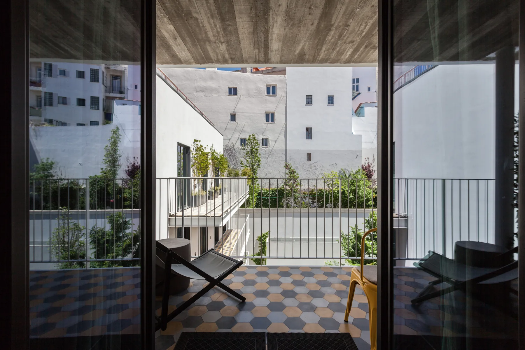 Un balcón con asientos da a edificios vecinos y un patio ajardinado.