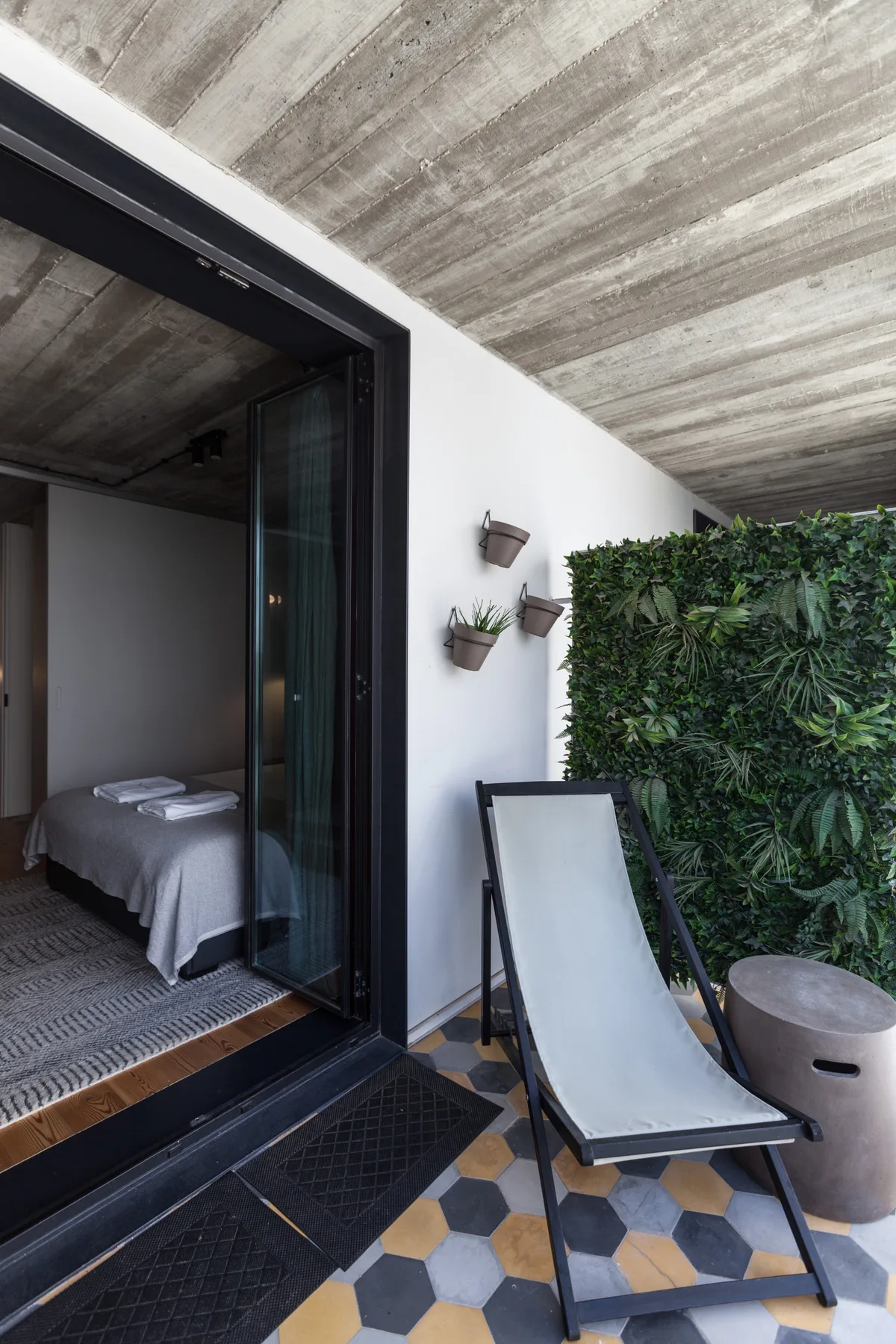 Un pequeño patio con una tumbona reclinable, plantas en macetas y una puerta abierta.