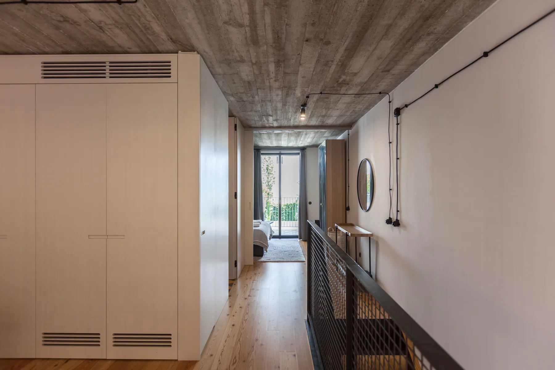 Un estrecho pasillo interior con suelo de madera conduce a una habitación luminosa.