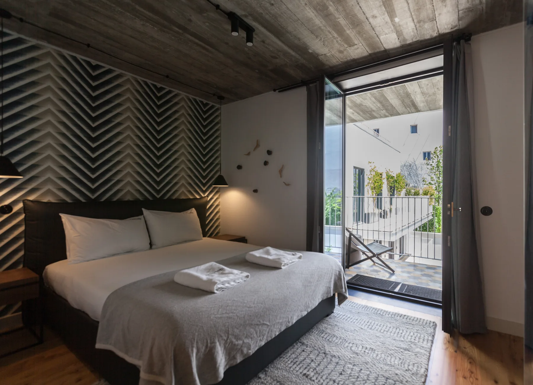 Un dormitorio con la cama hecha junto a una puerta de cristal abierta que da a un balcón.