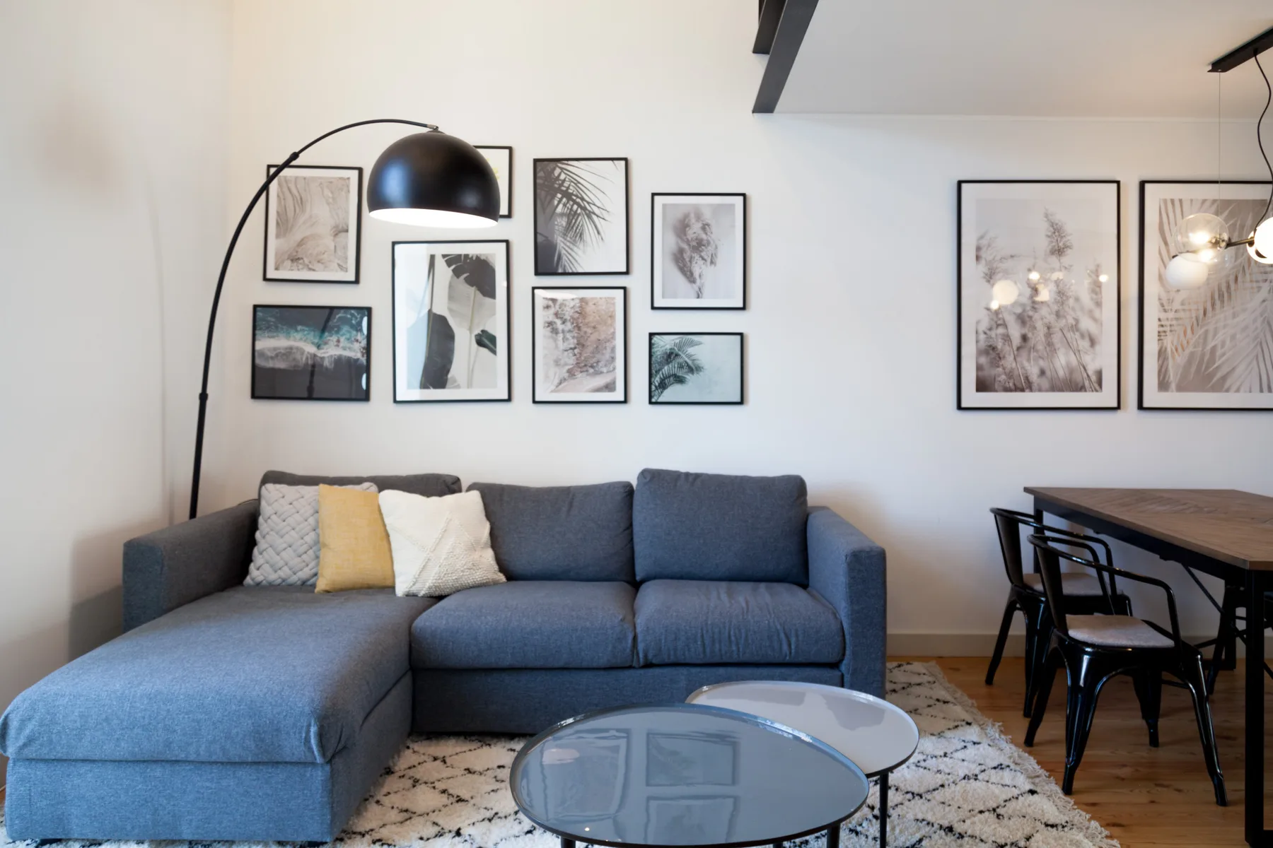 Una sala de estar con sofá seccional azul, cuadros enmarcados y mesa de comedor.