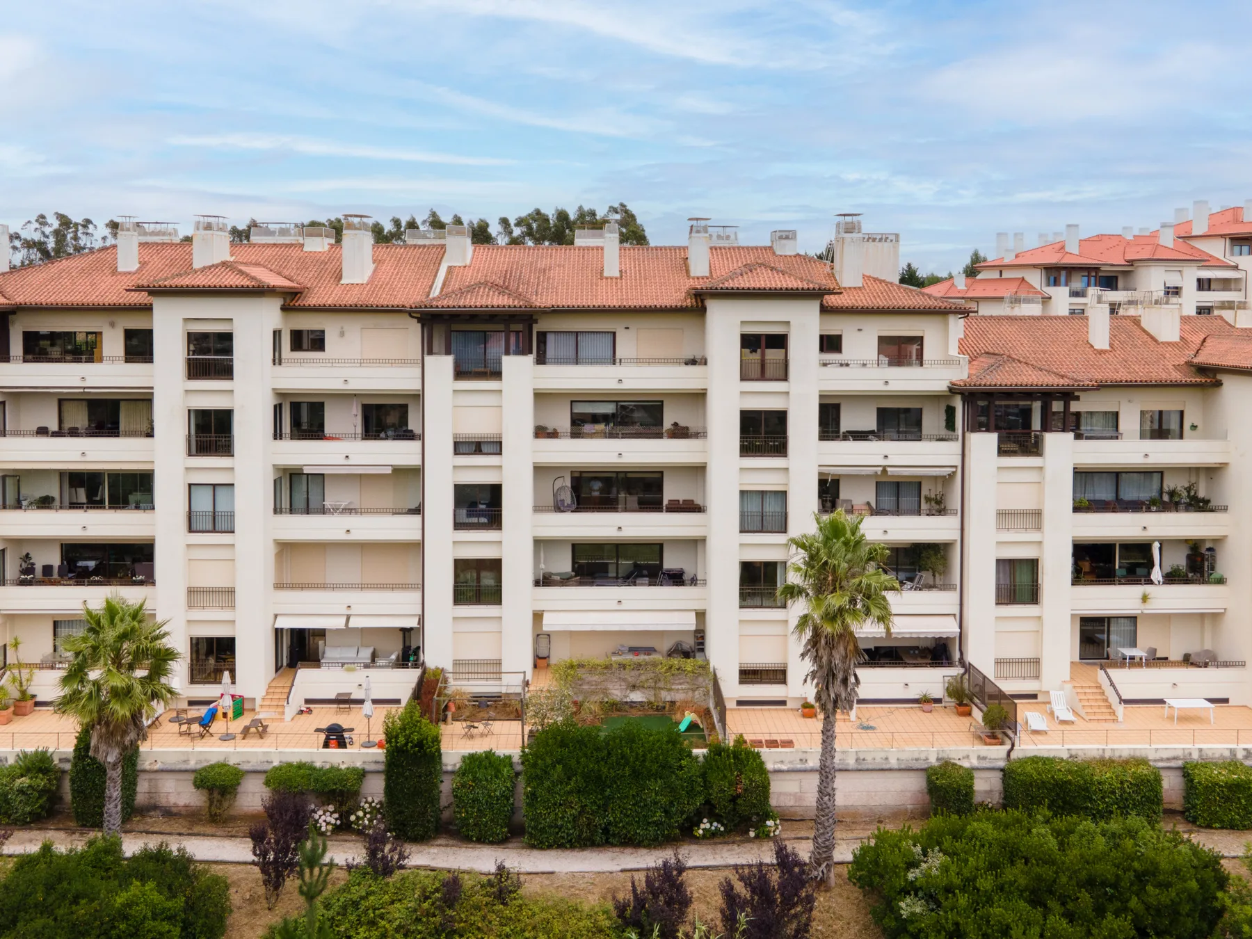 A multi-story residential building with balconies stands behind a landscaped garden.