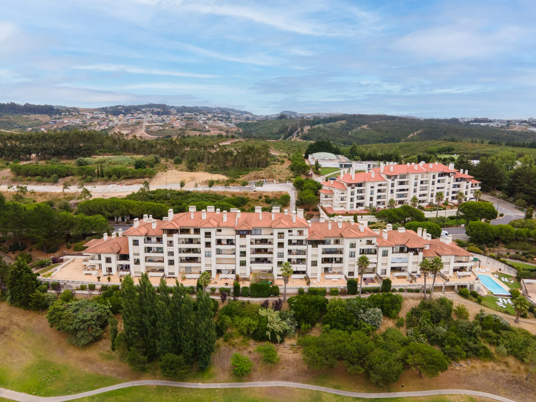 Aerial view of apartment buildings surrounded by greenery and rolling hills.