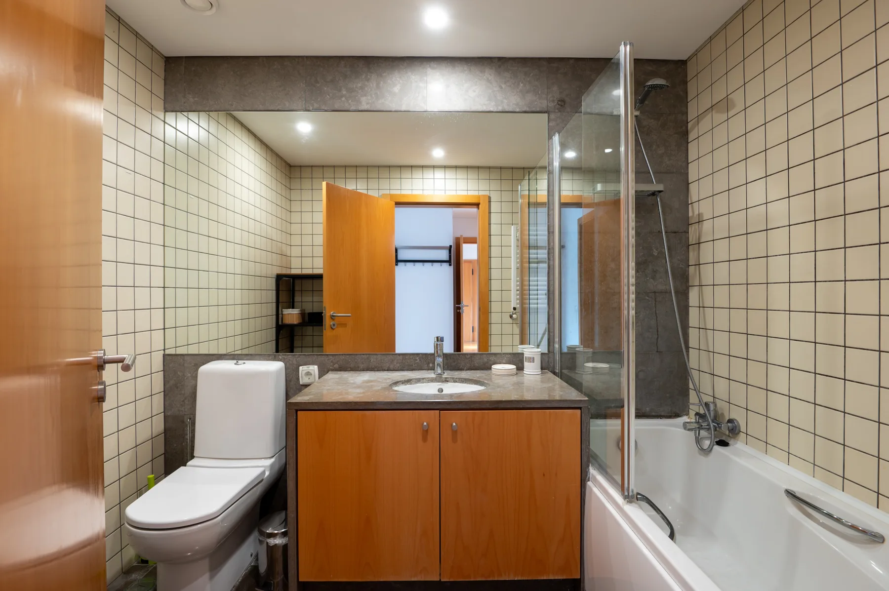 A tiled bathroom with a wooden vanity, toilet, and bathtub.