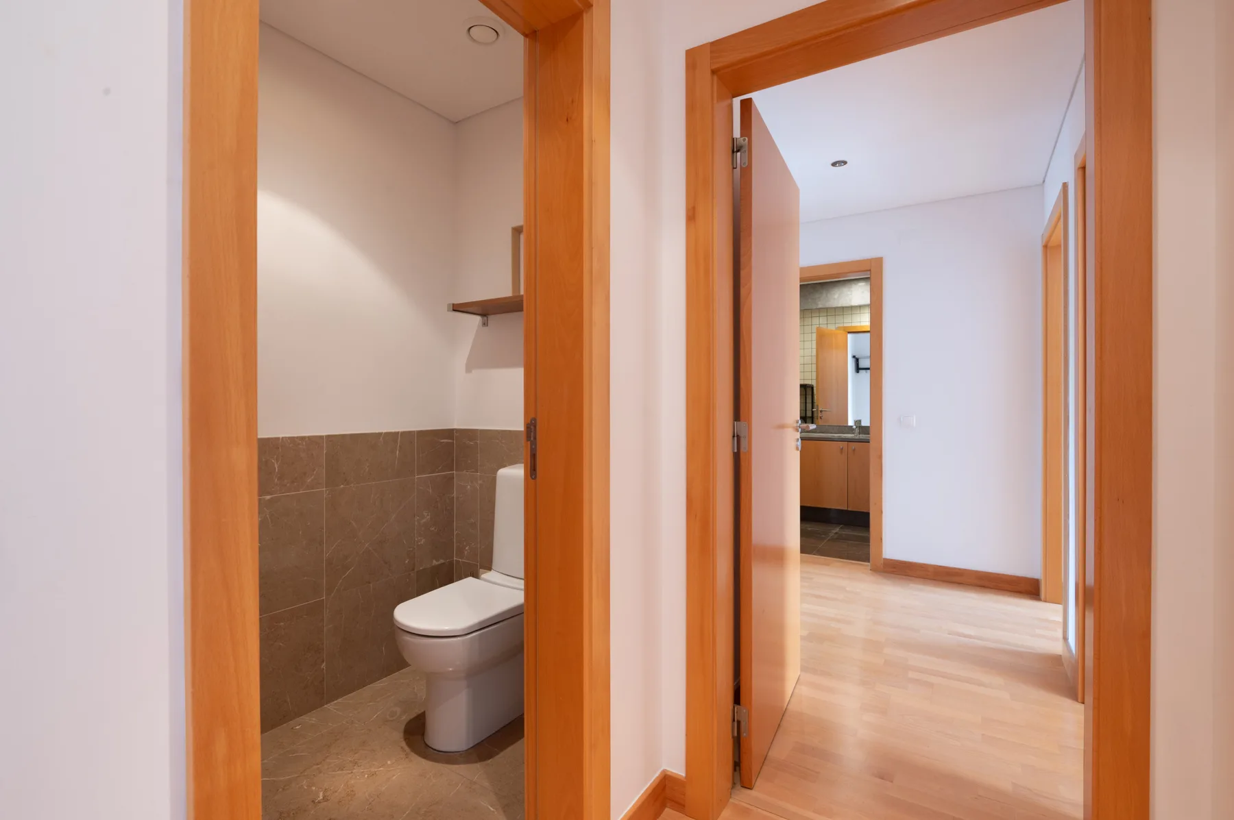 A hallway with an open bathroom doorway and light wood flooring.