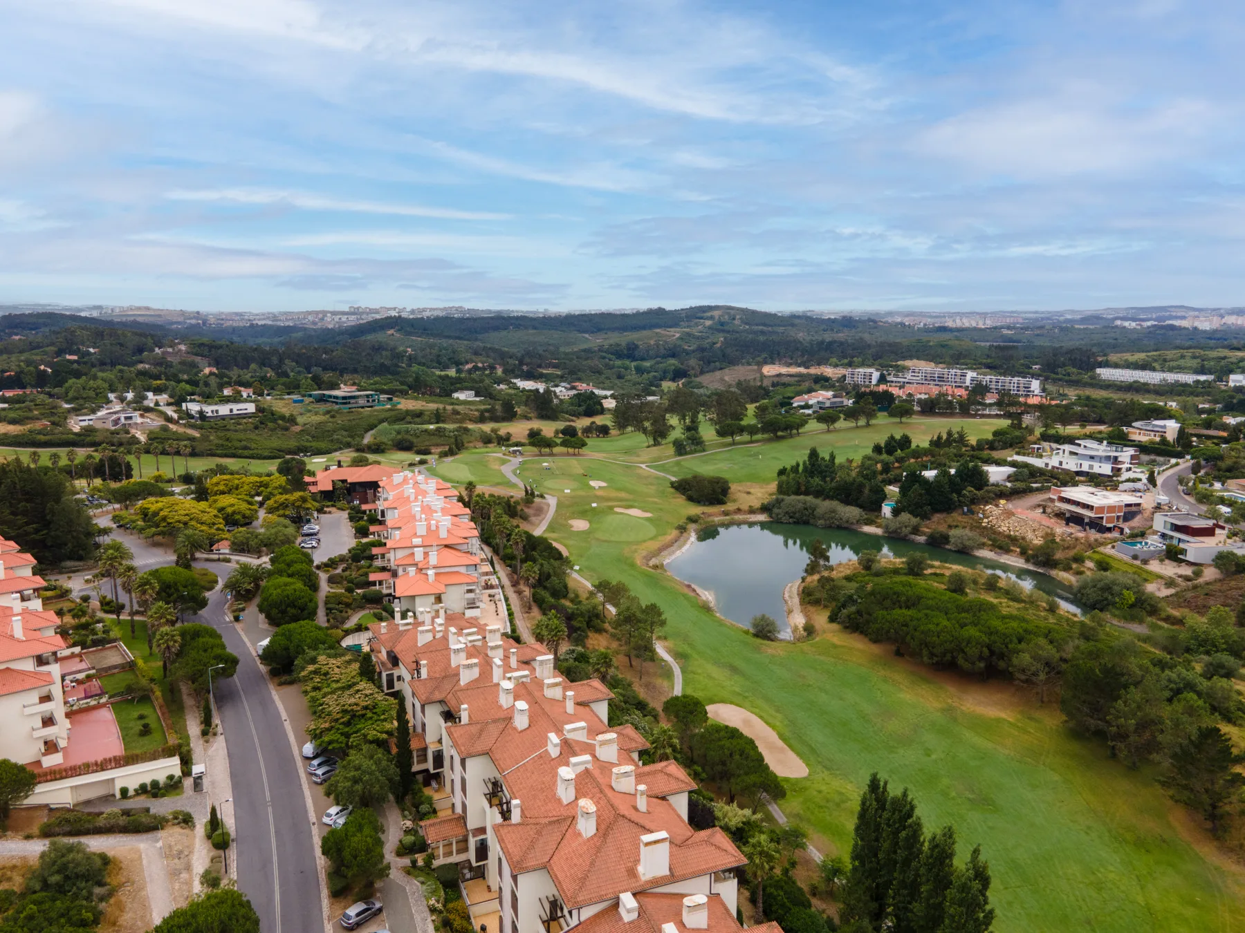 An aerial view of a golf course with a pond and nearby homes.