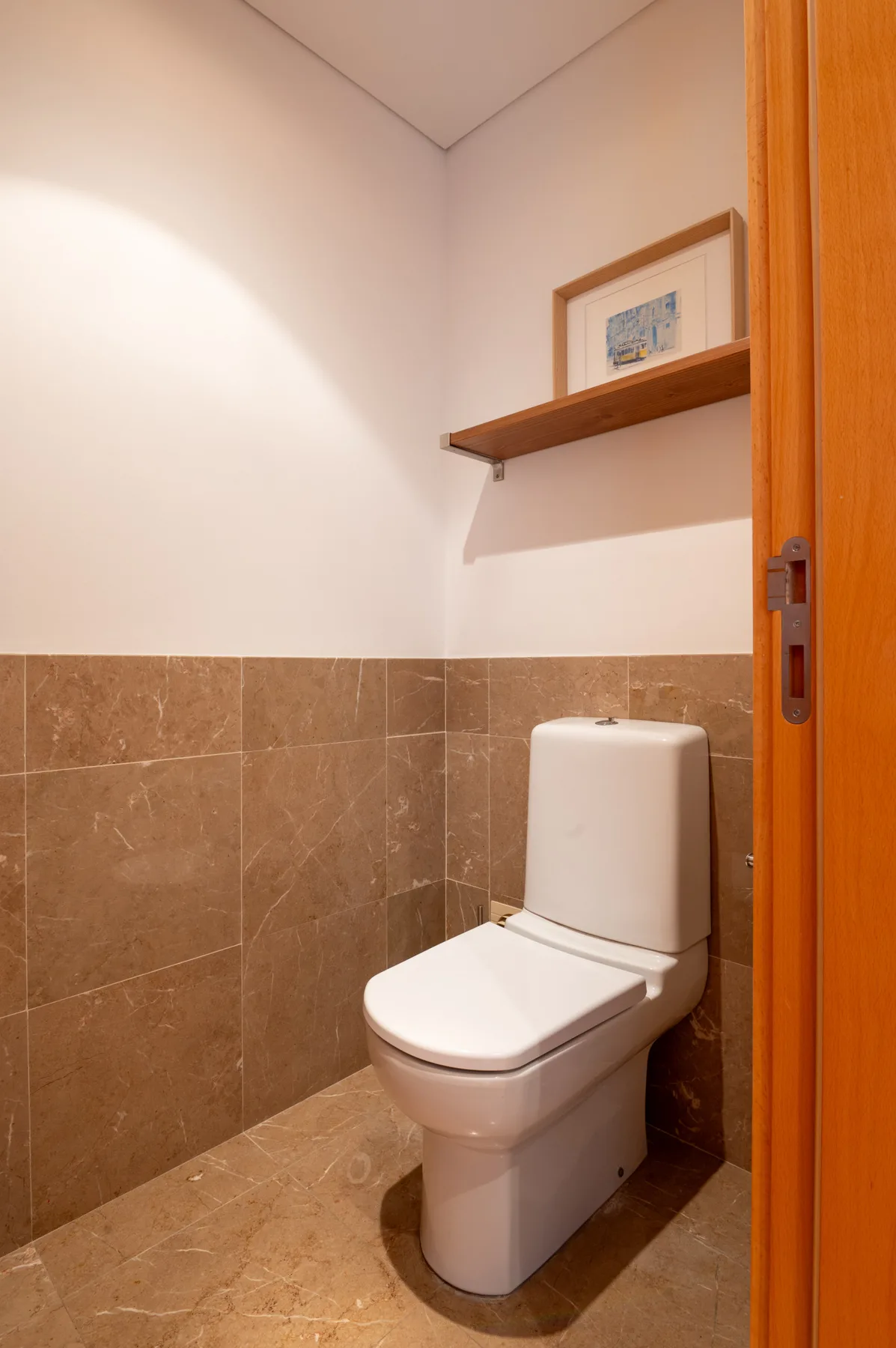 A small bathroom with a toilet and a wooden shelf.
