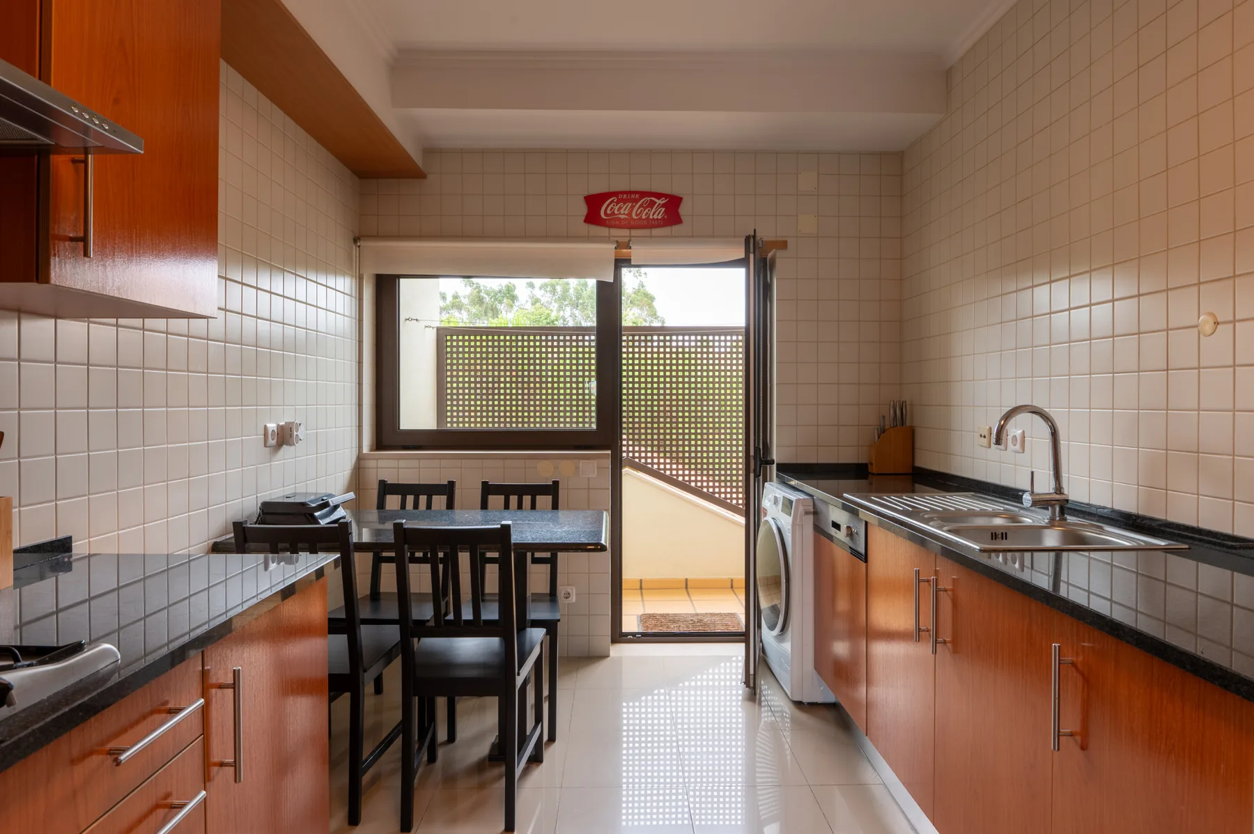 A tiled kitchen with a dining table beside a glass door opening onto a balcony.