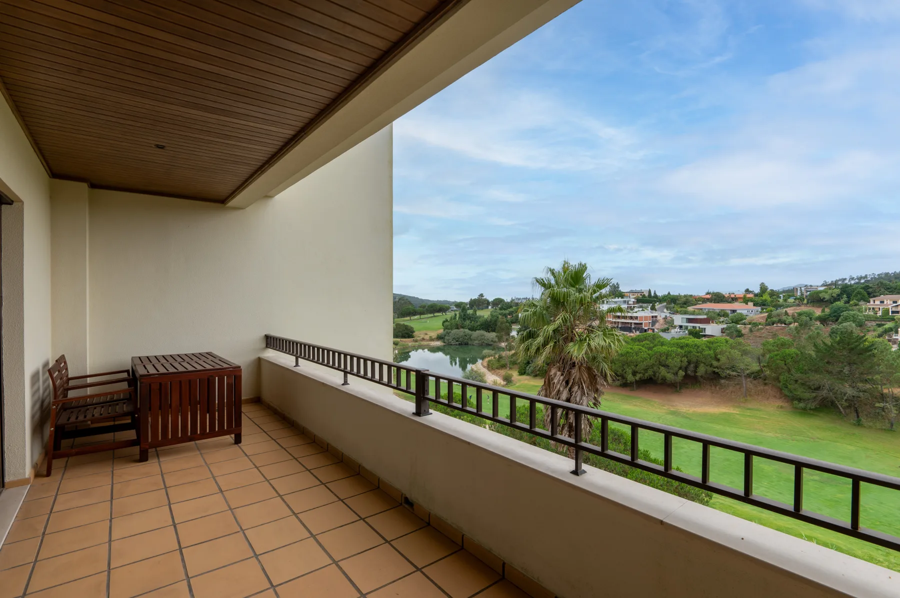 A covered balcony overlooks a green landscape, with seating beside the railing.
