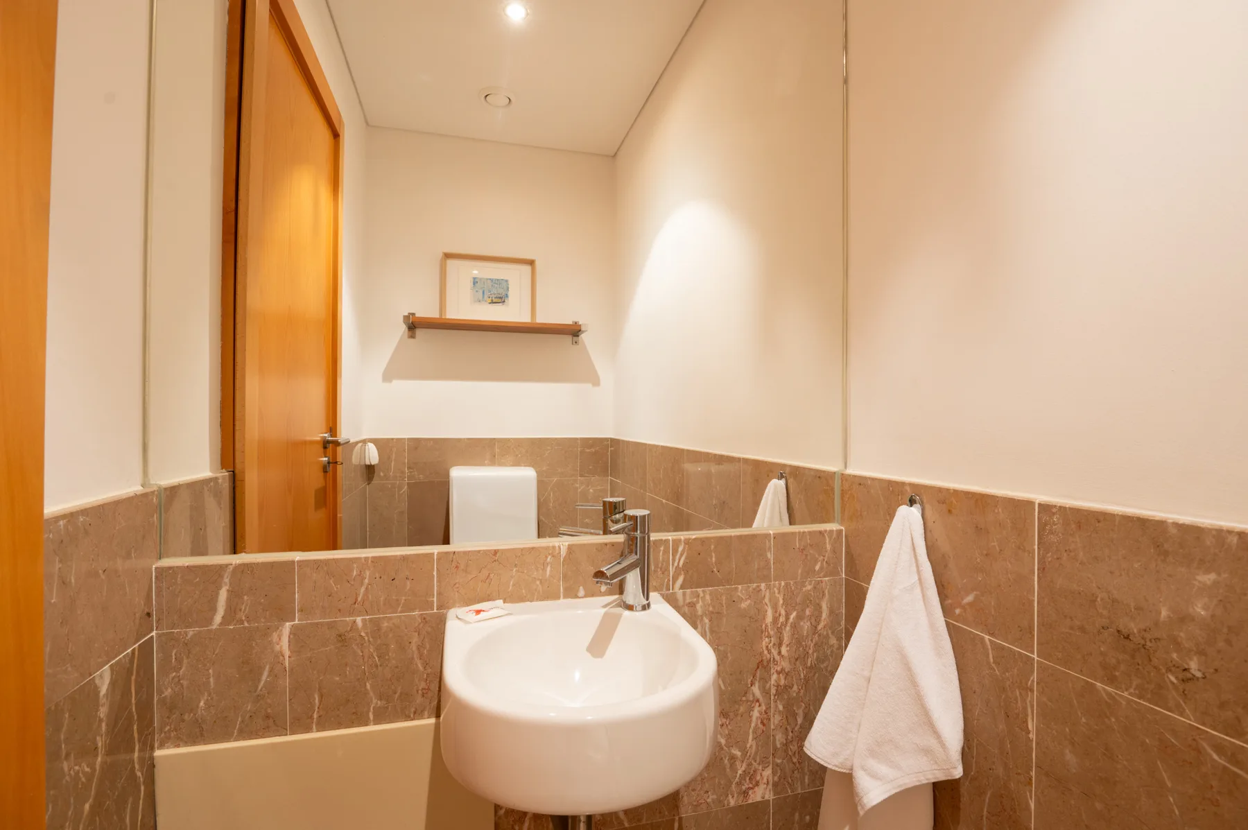 A bathroom vanity with a wall-mounted sink, mirror, and towel.