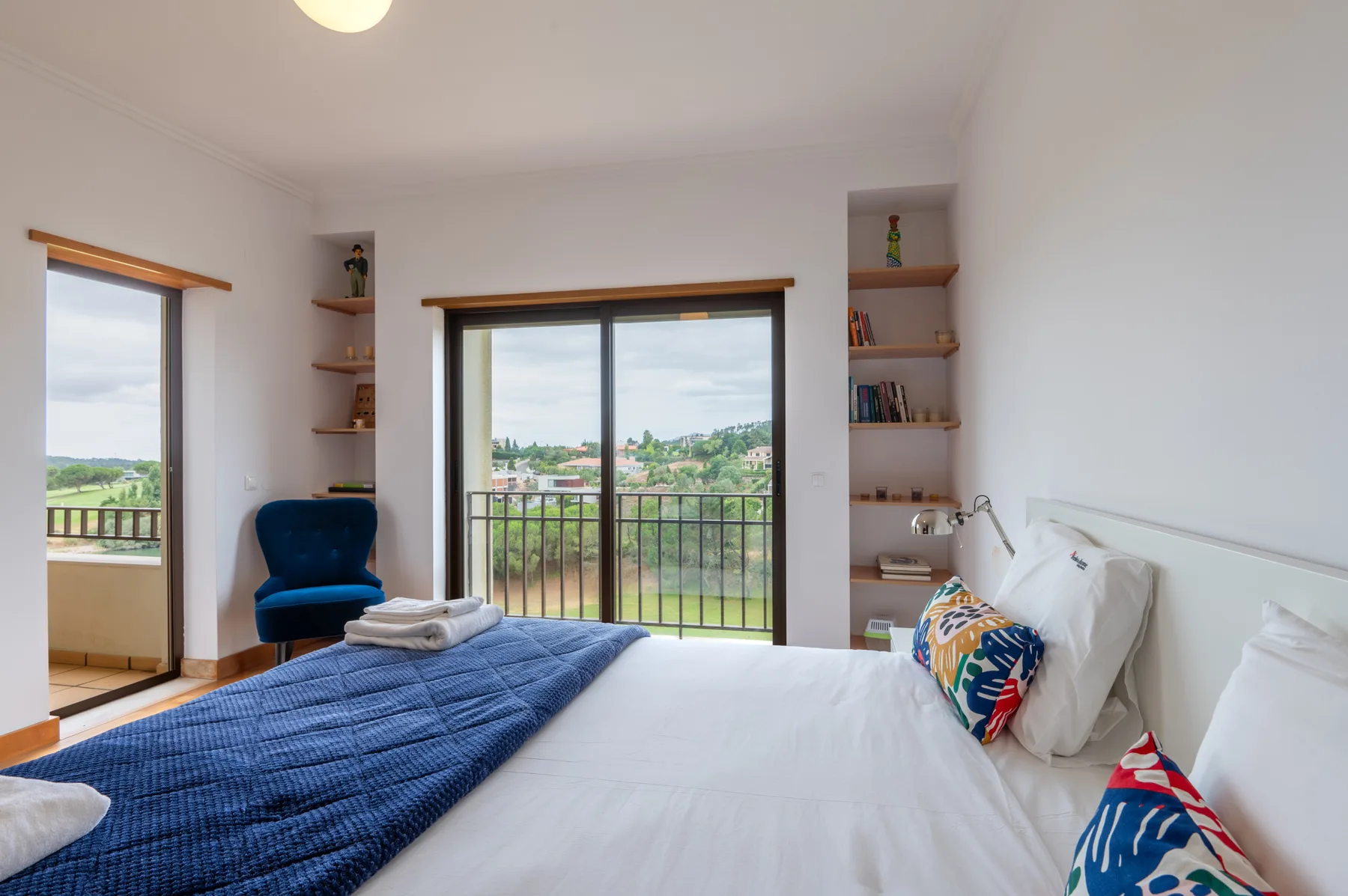 A bright bedroom with a bed beside sliding glass doors opening onto a balcony.