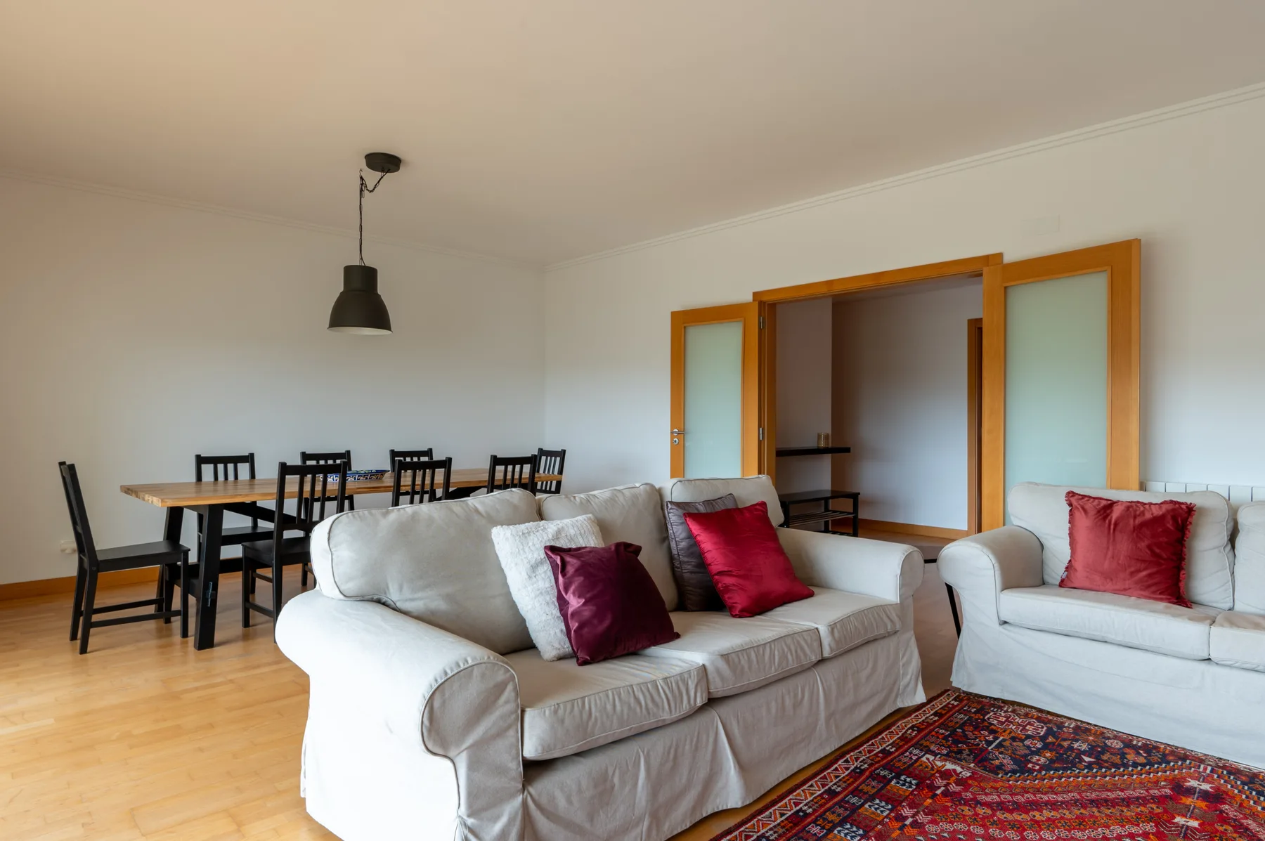 A bright living room with white seating, a dining table, and a patterned rug.