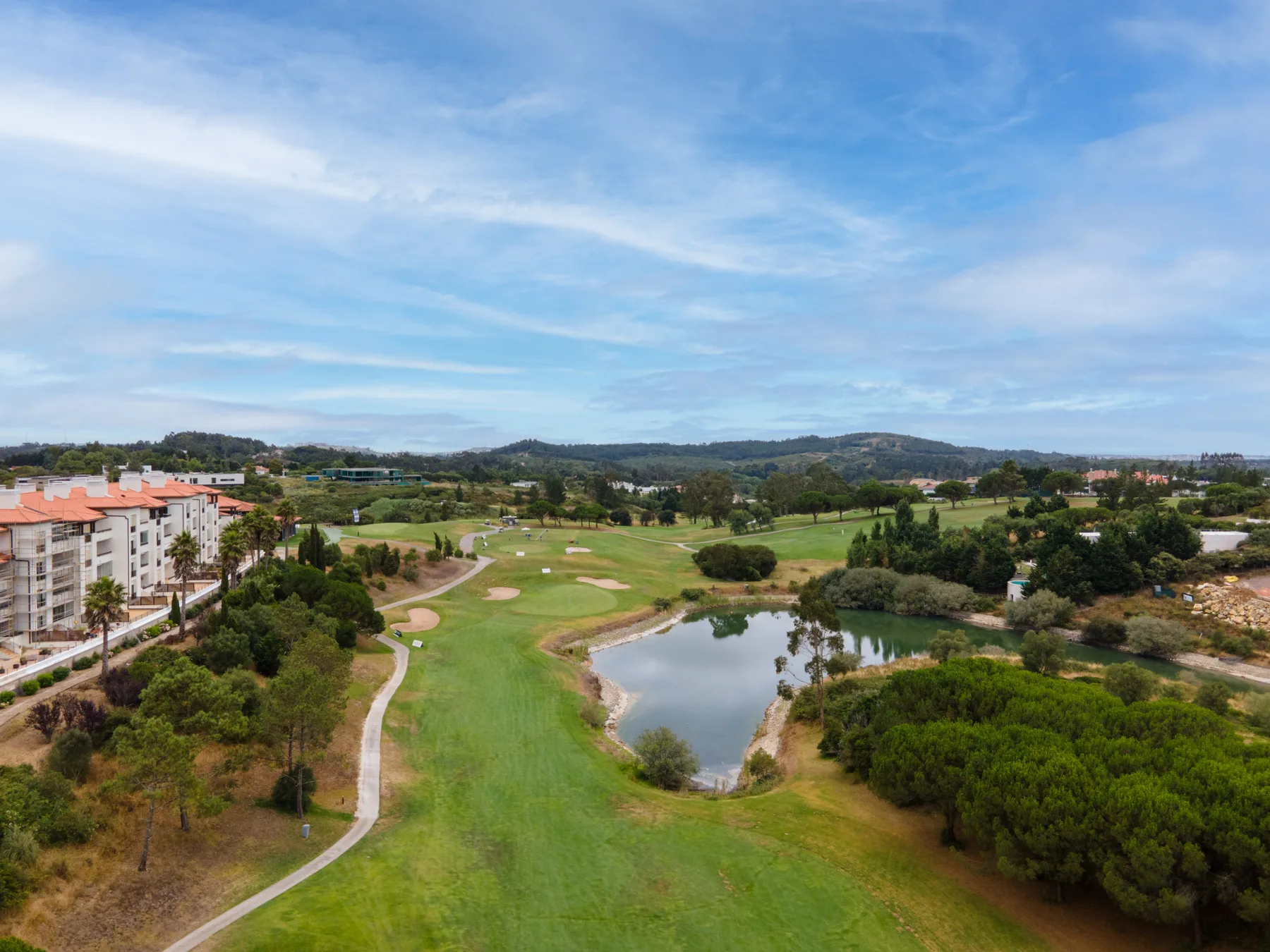 A golf course stretches across the landscape beside apartment buildings and a pond.