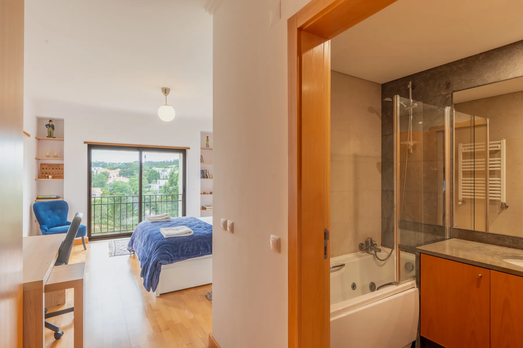 A bedroom with a bed and balcony doors opens beside a bathroom with a bathtub.