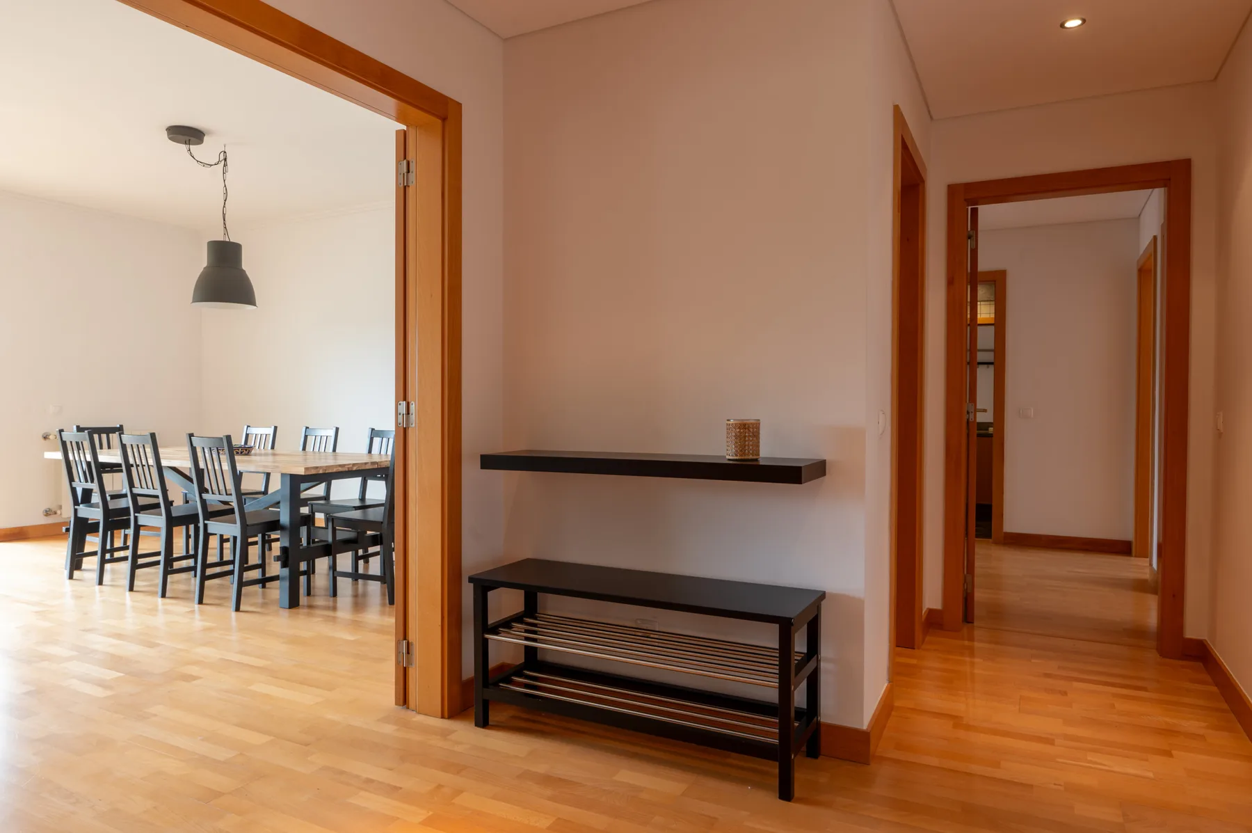 A wood-floored apartment hallway opens onto a dining area with a table and seating.