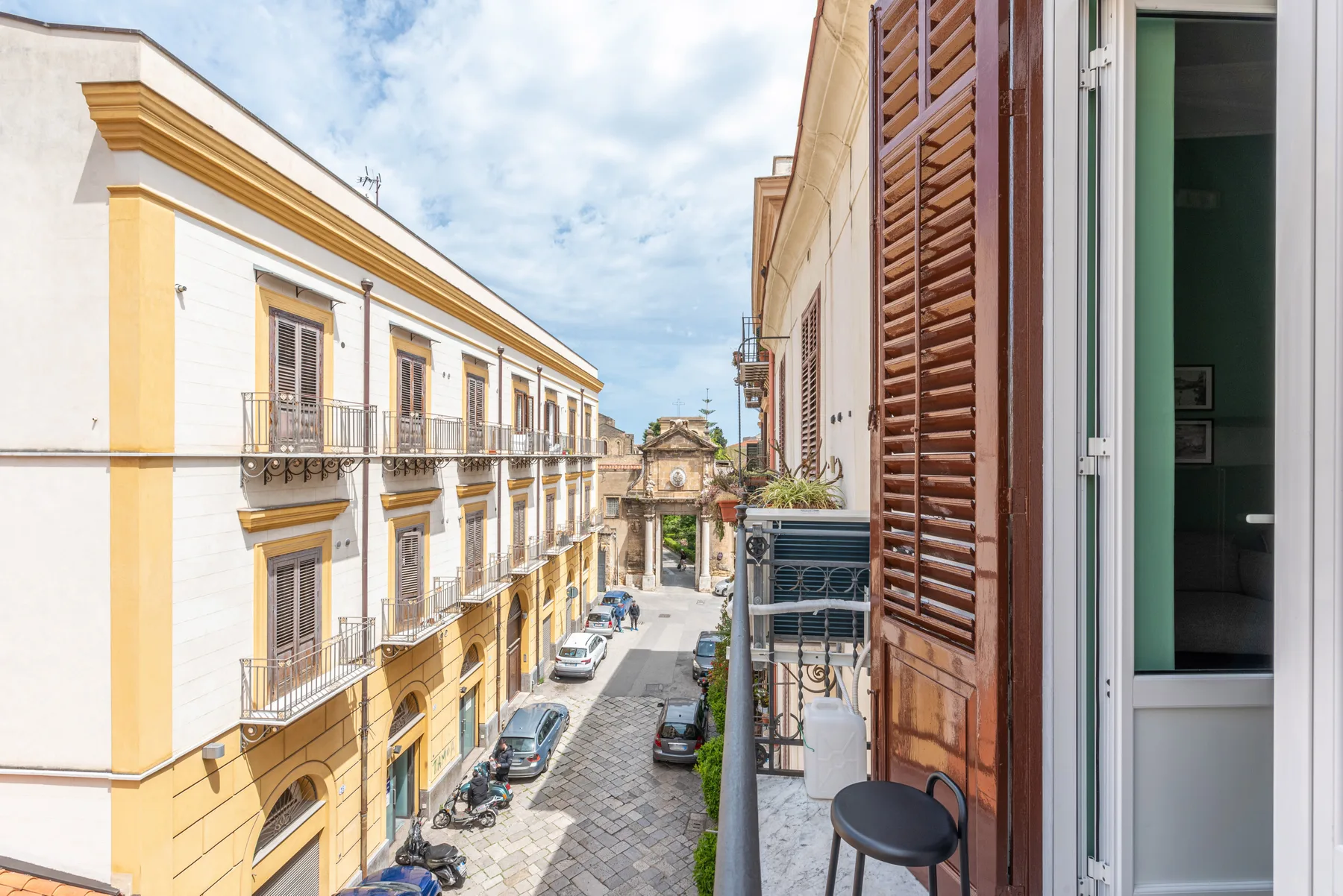 Una calle estrecha vista desde un balcón, con edificios y vehículos estacionados.