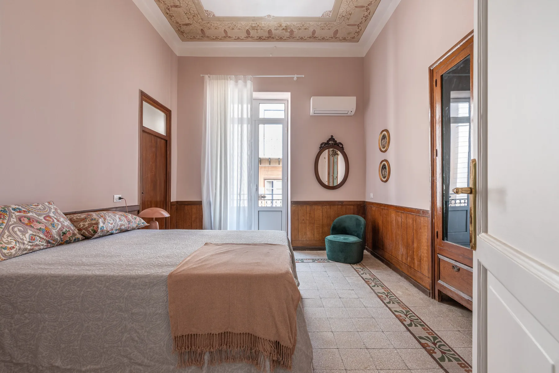 Un dormitorio con una cama, una puerta acristalada con cortina y un pequeño asiento tapizado.