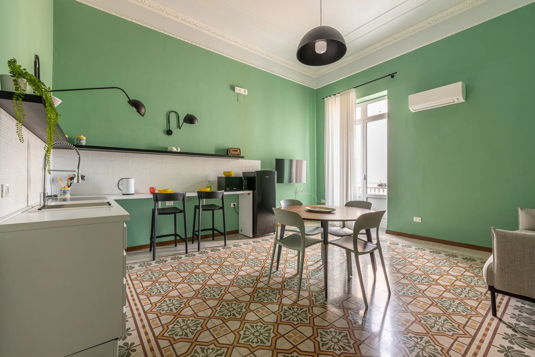 Una cocina y comedor de paredes verdes con mesa, sillas y suelo de azulejos estampados.