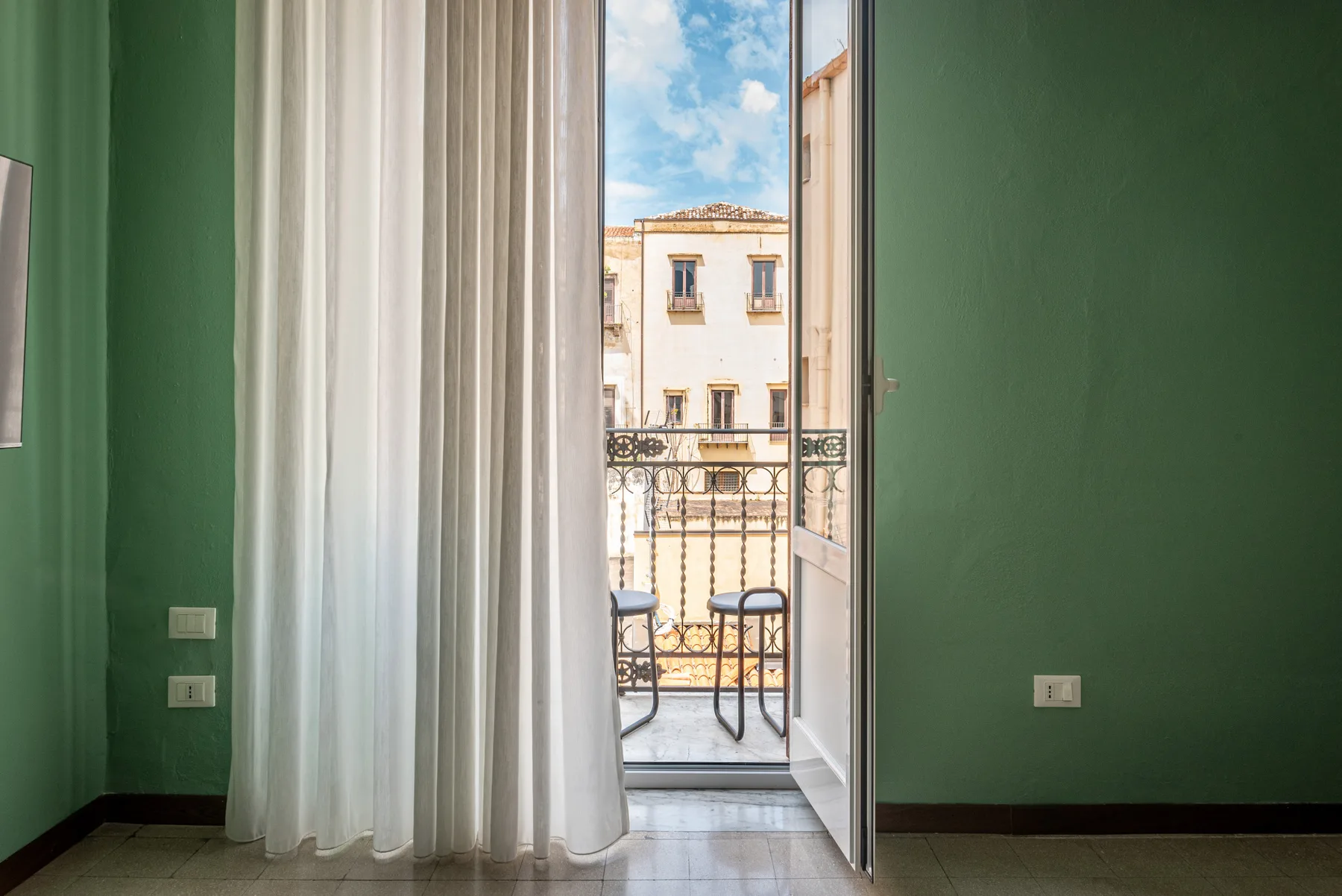 Una habitación verde da a un pequeño balcón a través de una puerta de vidrio.