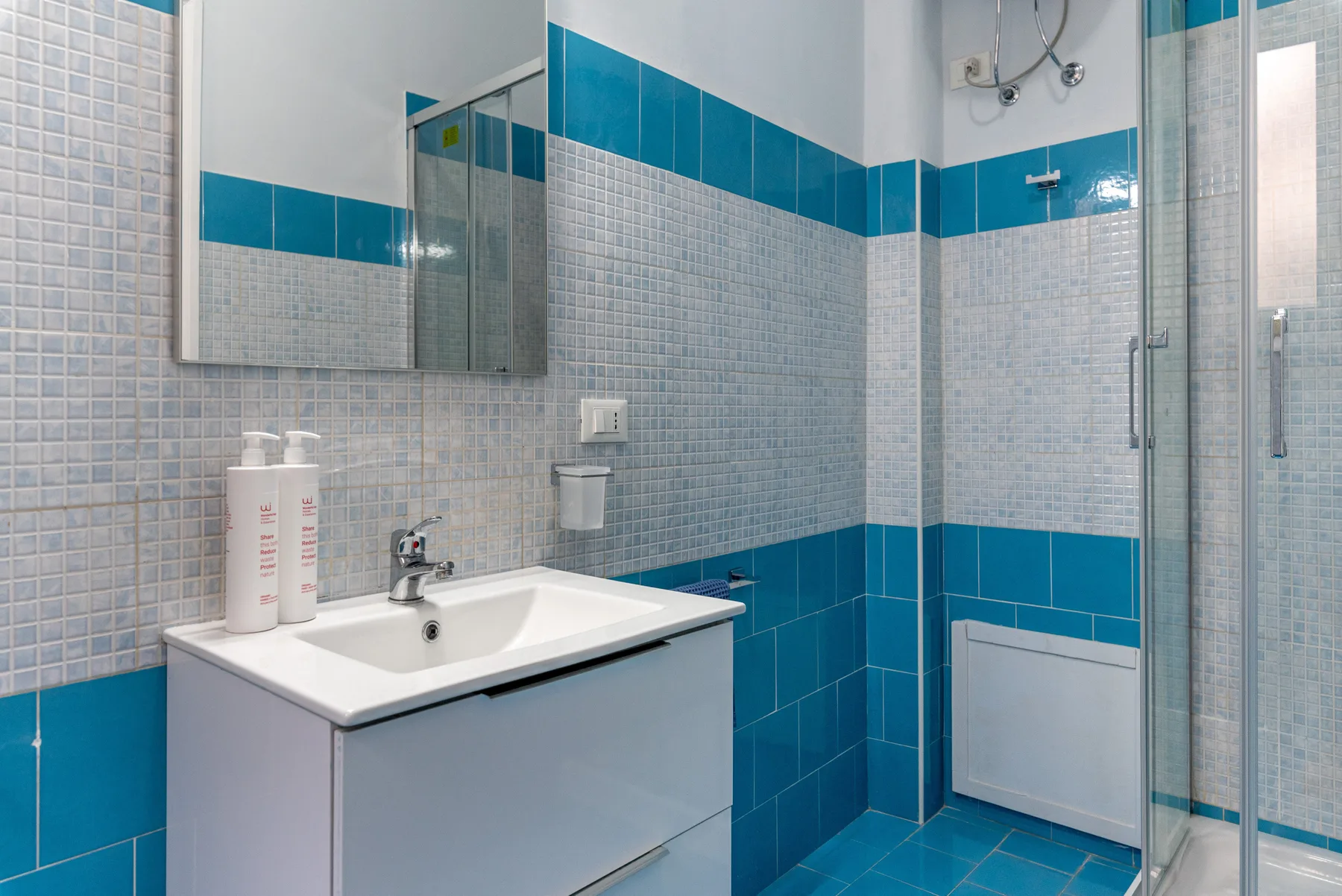 Un baño alicatado con lavabo, espejo y ducha.