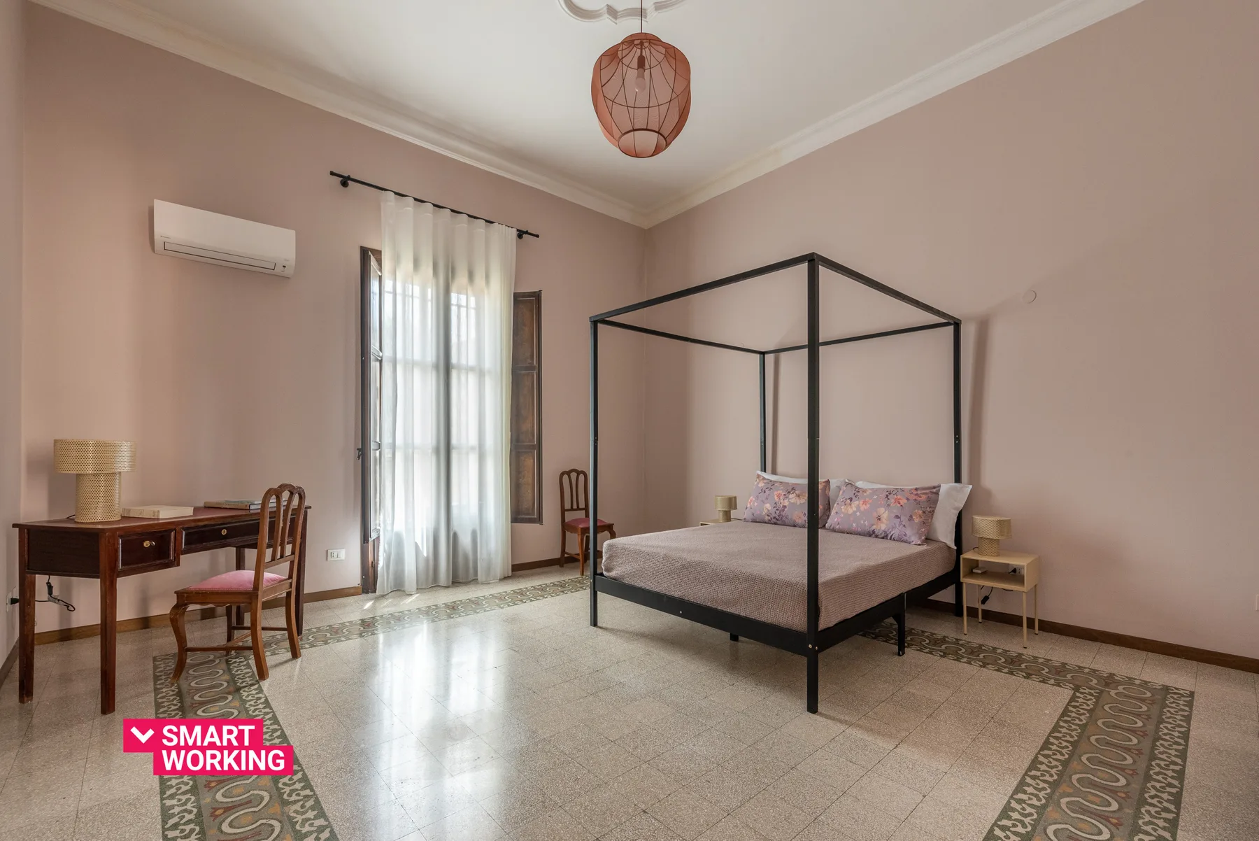 Un dormitorio con una cama con dosel, un escritorio y una ventana alta con cortinas.