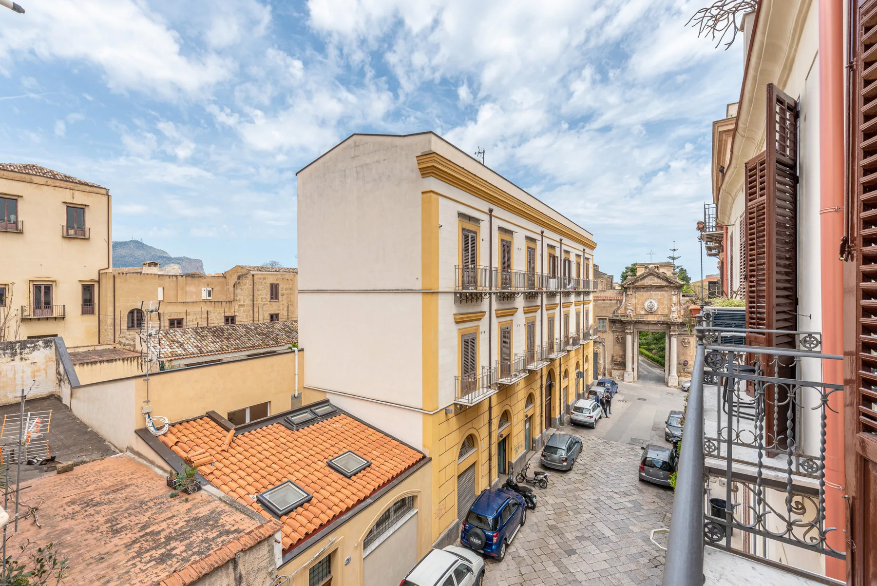 Una calle flanqueada por edificios históricos, vista desde un balcón bajo un cielo parcialmente nublado.